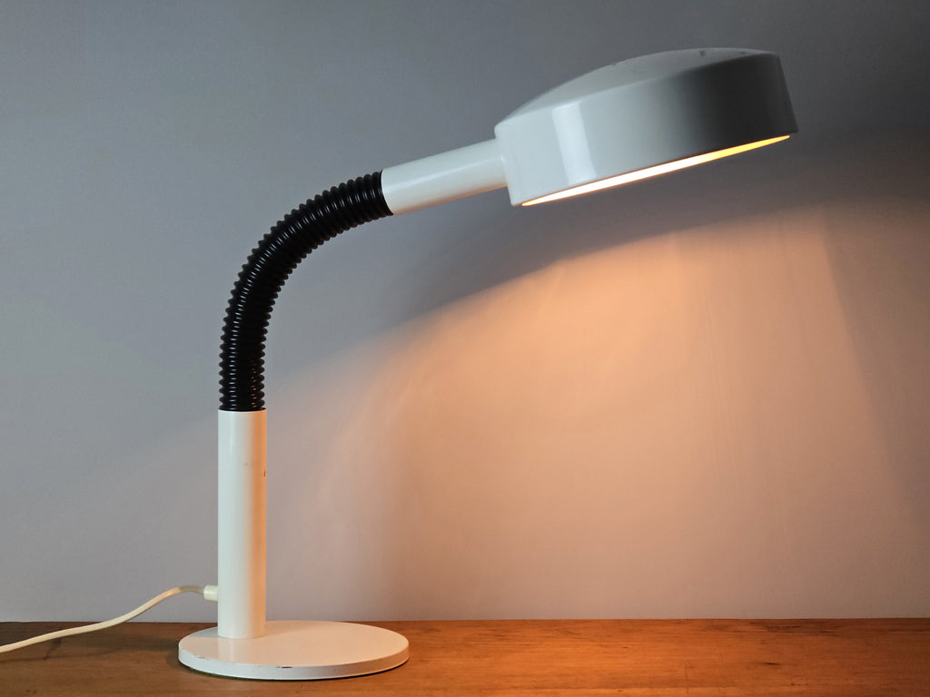 1960s Mid Century Modern gooseneck desk lamp by Hala Zeist, profile view of the lamp lit, on a vintage wooden table, the background is slightly darker than the previous lit image.