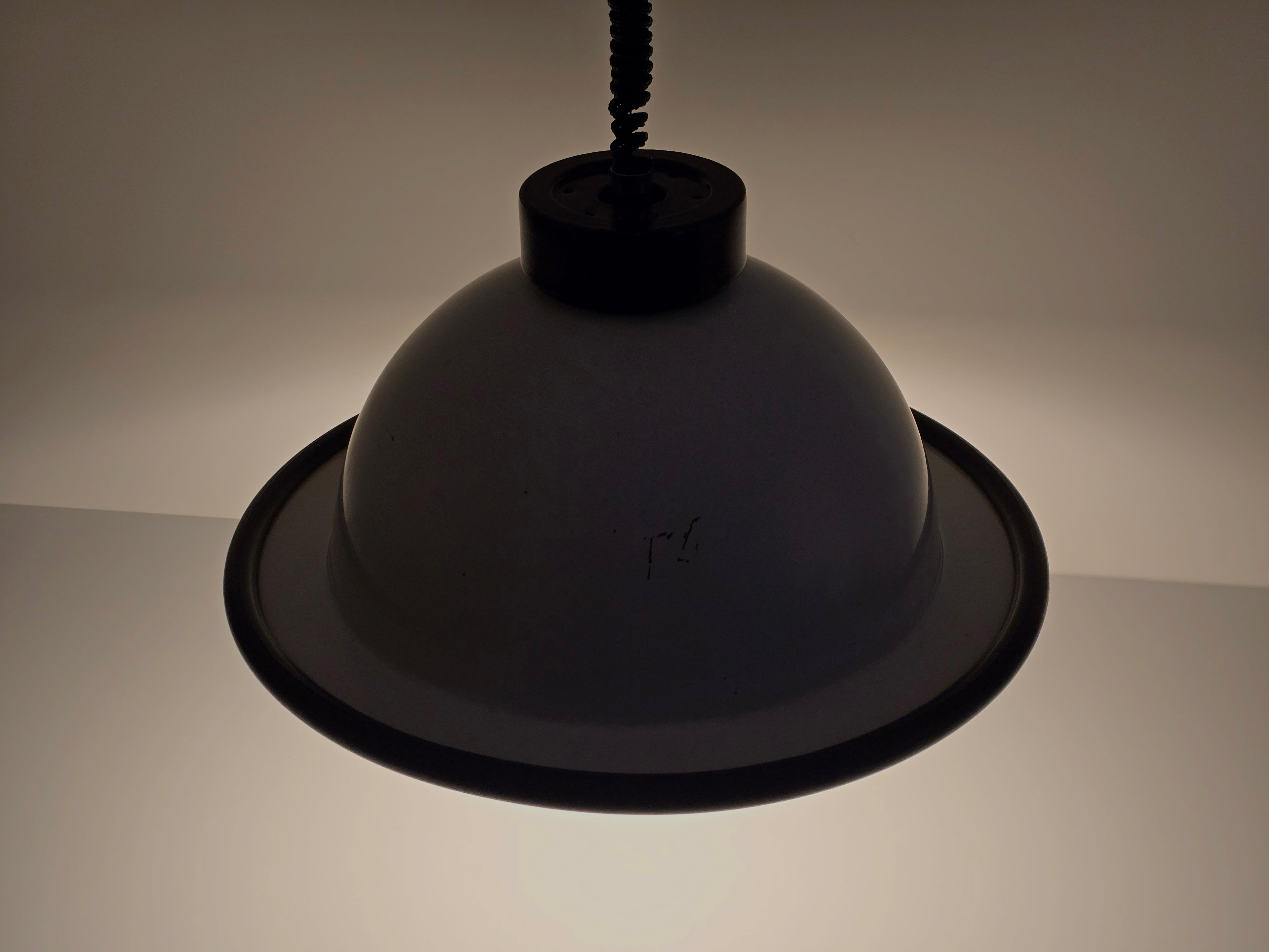 The vintage 1960s MCM Martinelli Luce rise & fall pendant lamp by Elio Martinelli shown in a darkened setting, top down view, to highlight the shape of the lamp.