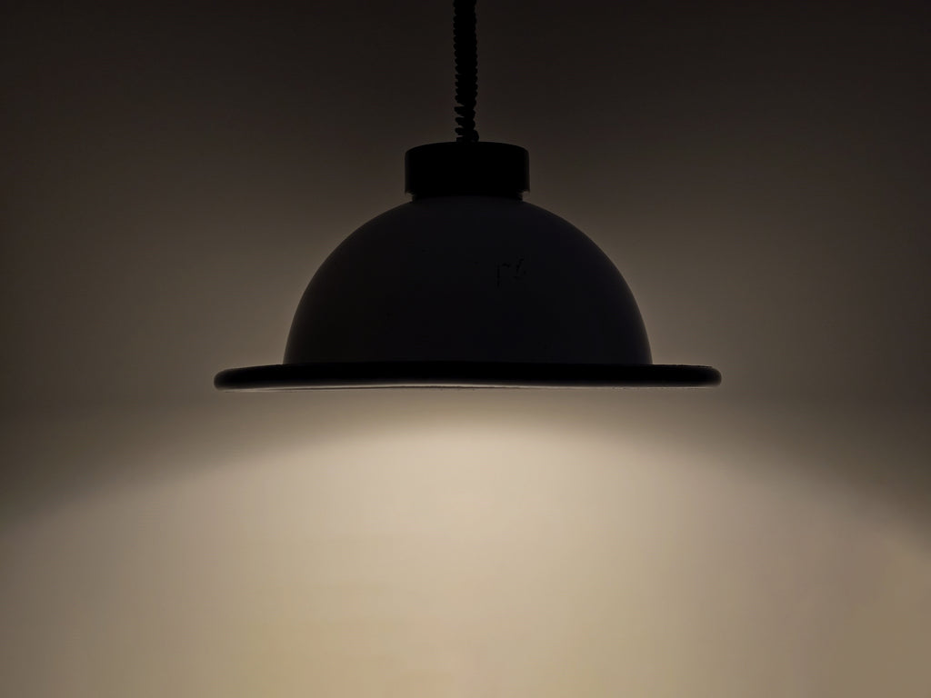 The vintage 1960s MCM Martinelli Luce rise & fall pendant lamp by Elio Martinelli shown in a darkened setting to highlight the shape of the beam.