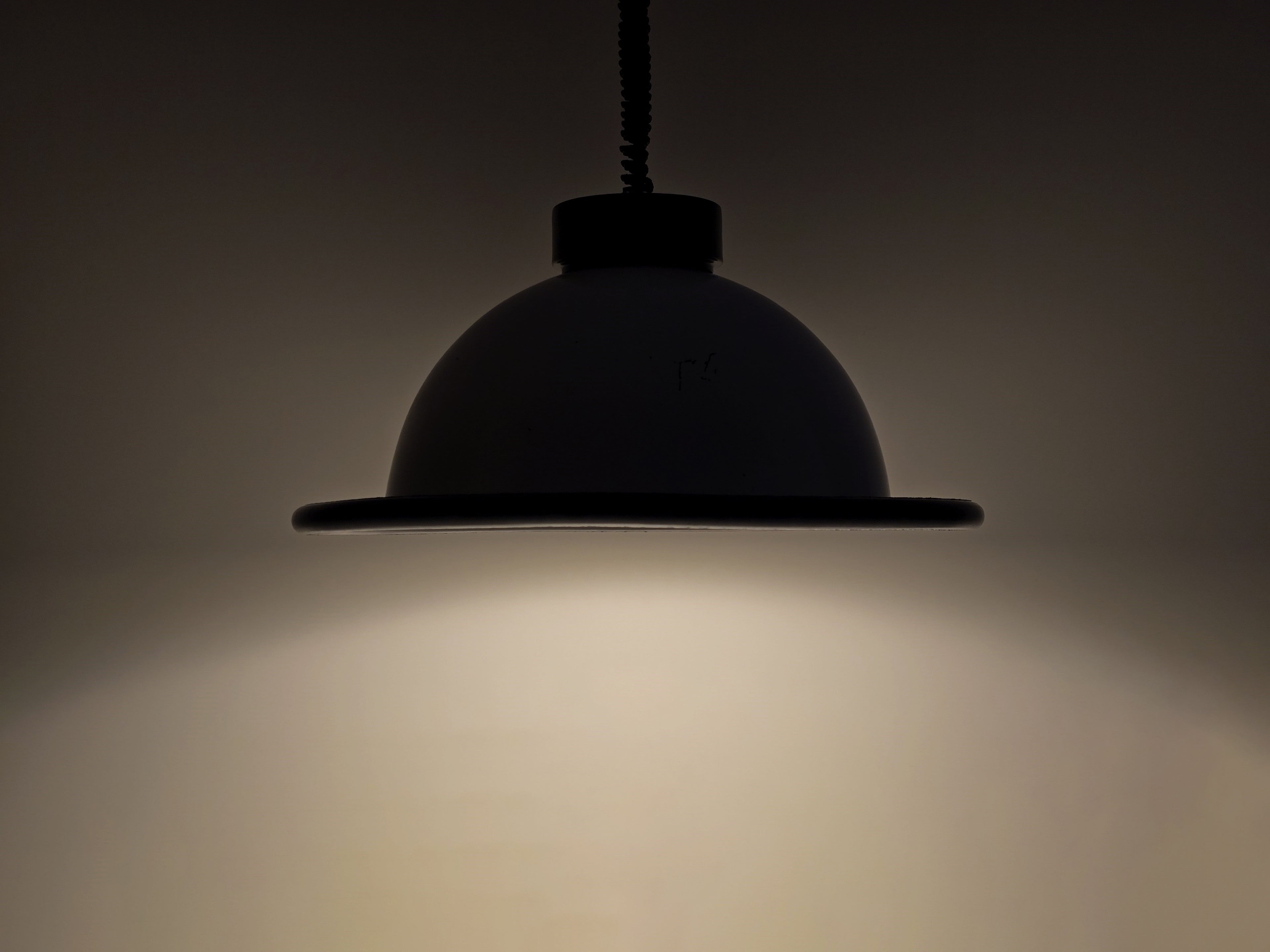 The vintage 1960s MCM Martinelli Luce rise & fall pendant lamp by Elio Martinelli shown in a darkened setting to highlight the shape of the beam.