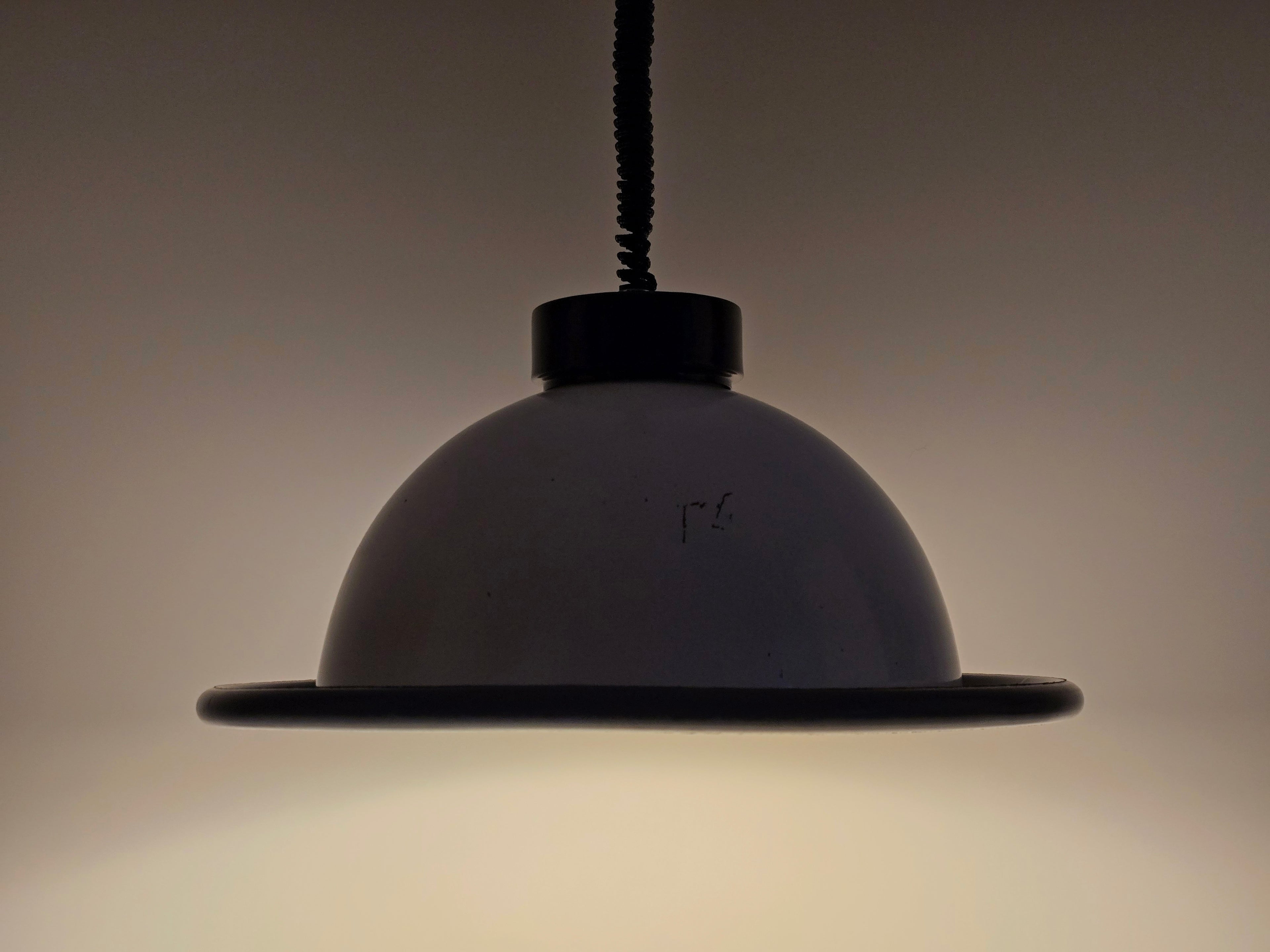 A moody shot of the vintage 1960s MCM Martinelli Luce rise & fall pendant lamp by Elio Martinelli with the light on, emphasizing its ambient glow.