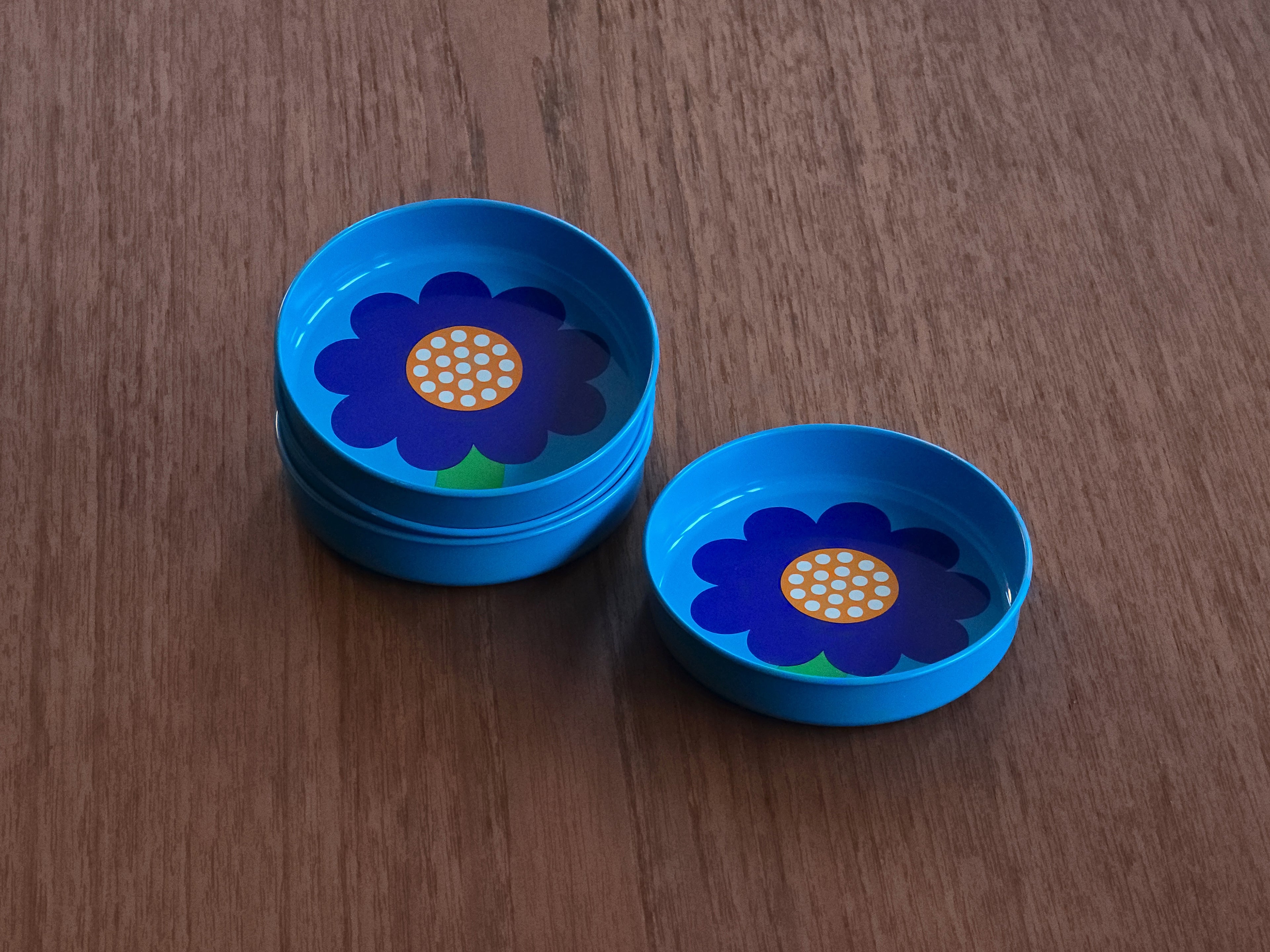 Top down perspective image of four vintage 1970s Laurids Lønborg tin trays designed by Al and Lena Eklund, styled image of 3 trays stacked and the fourth on a teak table next to the others.