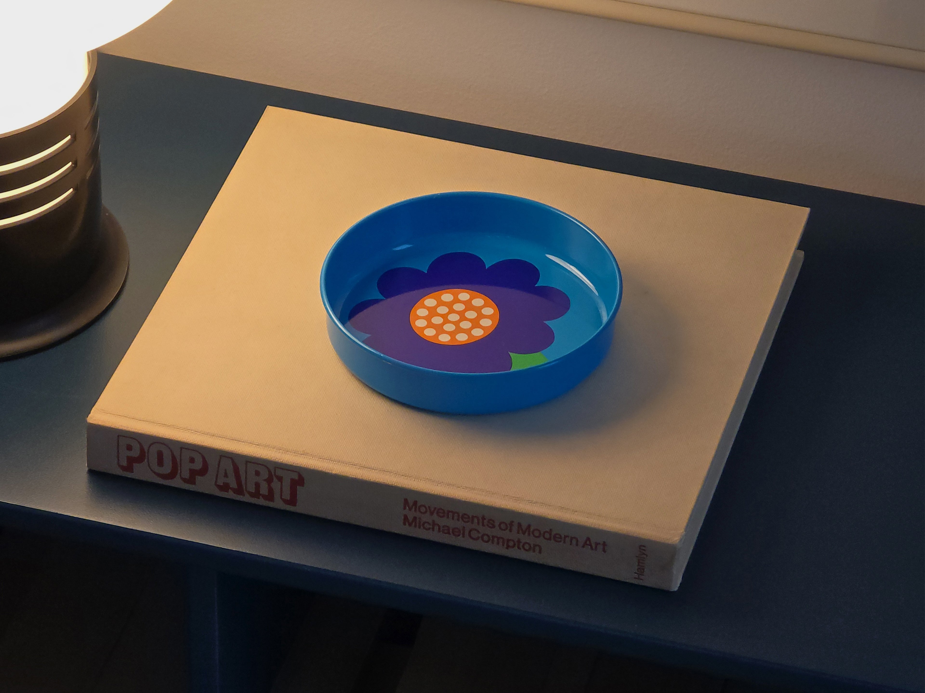 Top down image of a vintage 1970s Laurids Lønborg tin tray designed by Al and Lena Eklund, styled image on a book, set on a blue cabinet.