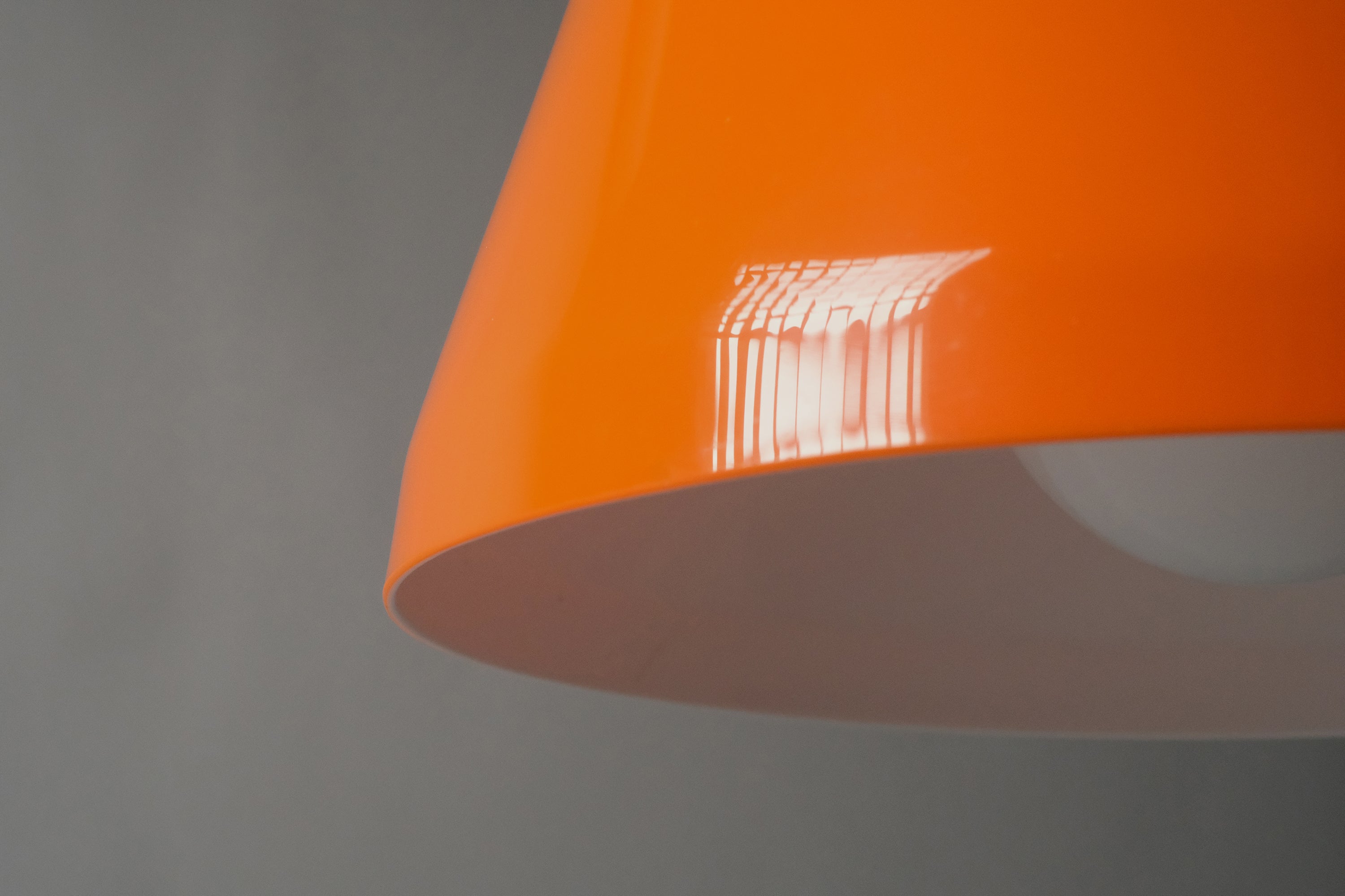 Close-up of the lower edge of a 1970s orange acrylic Space Age pendant lamp, revealing the precise bonded transition between the glossy orange exterior and white interior layer.
