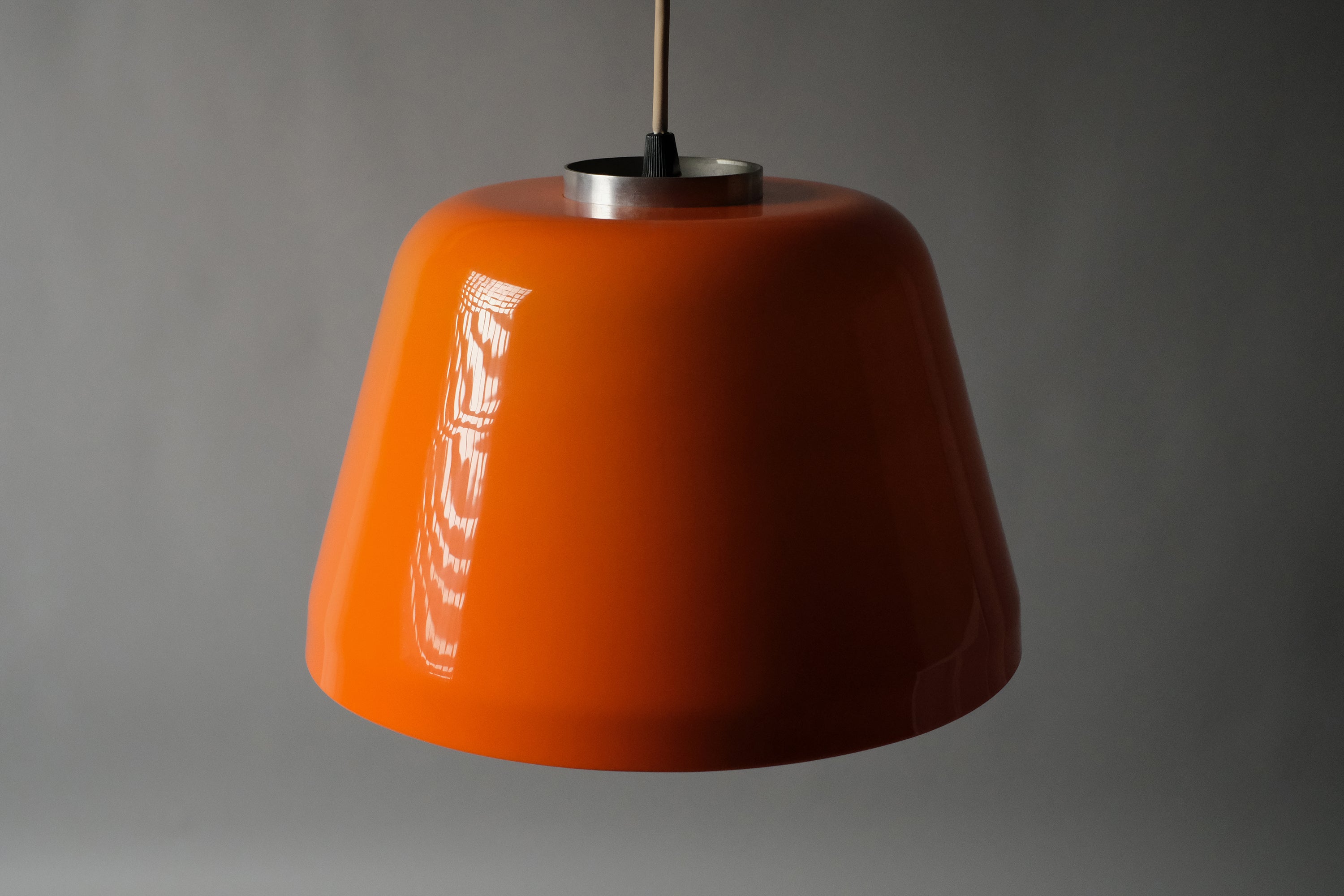 High-angle view of a 1970s orange acrylic Space Age pendant lamp suspended on cord, emphasizing the tapered dome form and deep orange color from above.