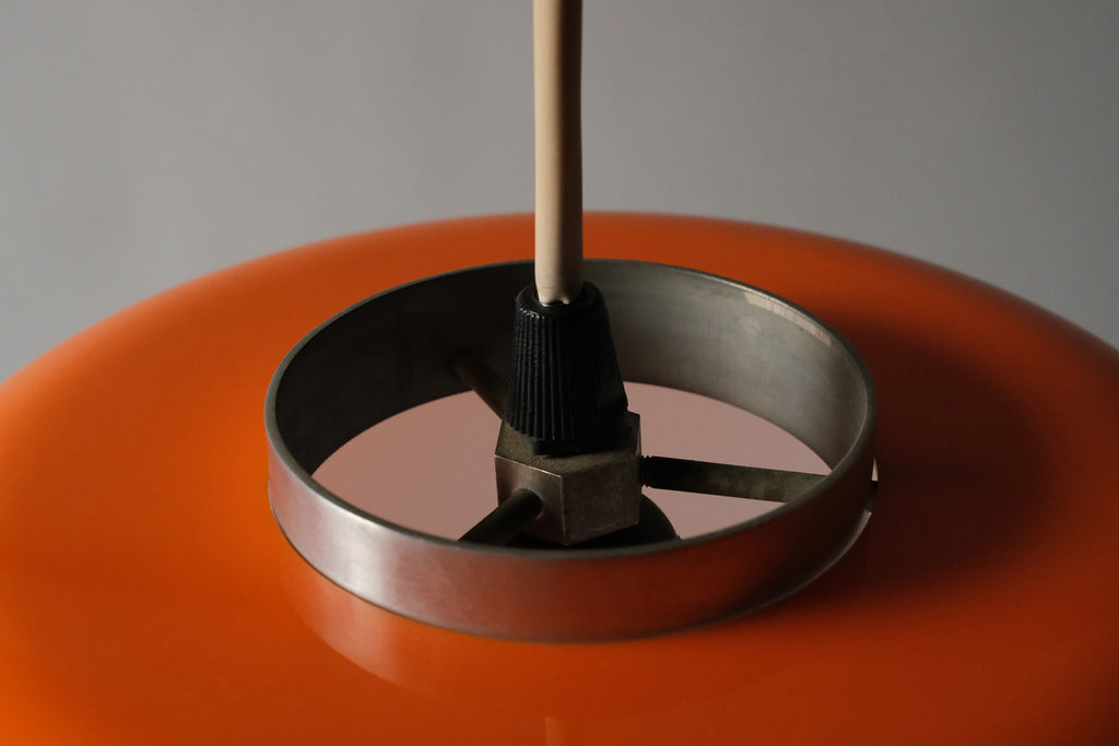 Macro detail of the ceiling fitting and cord entry point of a 1970s orange acrylic Space Age pendant lamp, showing the original hardware and suspension mechanism.