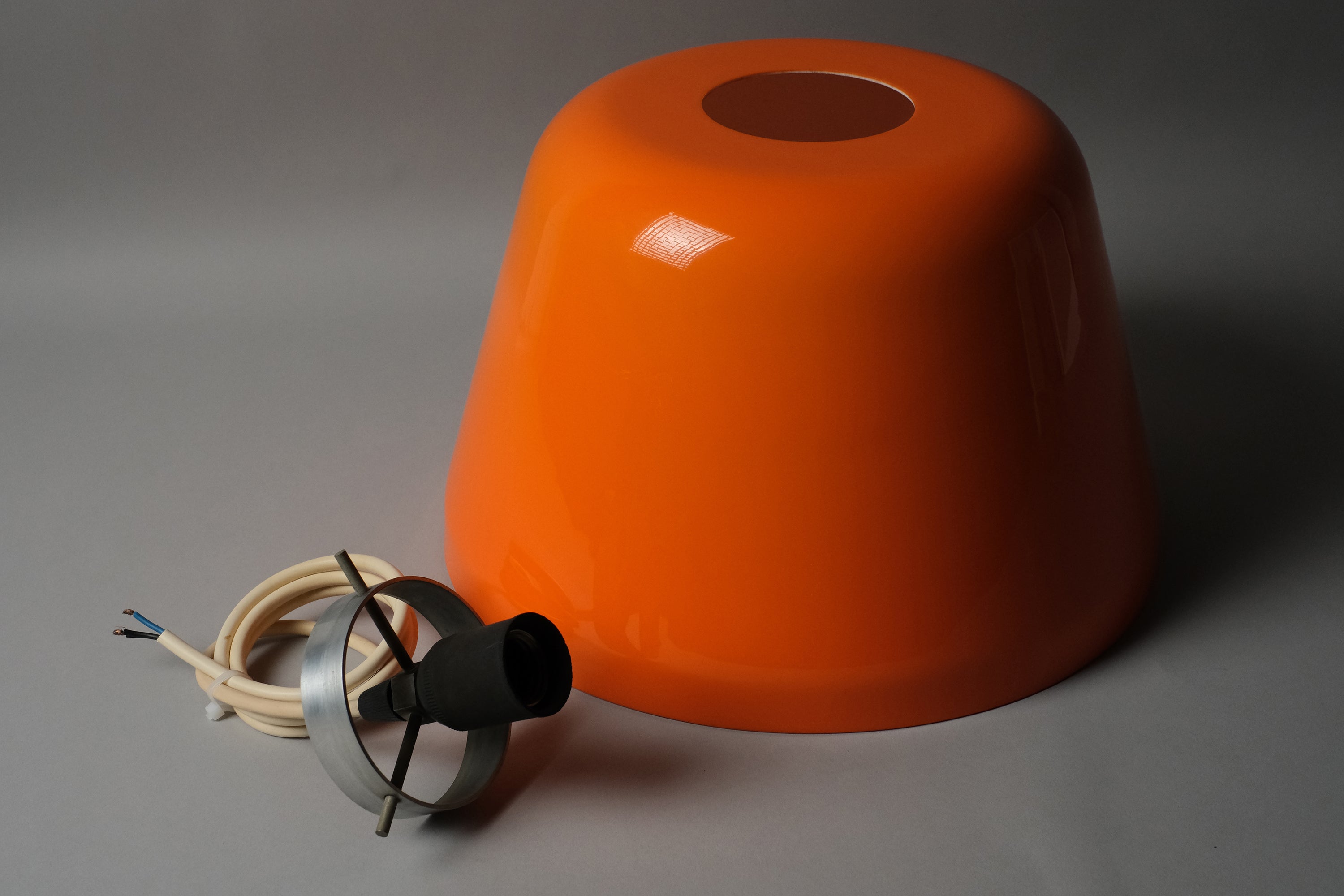Inverted view of a 1970s orange acrylic Space Age pendant lamp resting upright, with original cord and E27 fitting visible alongside the shade exterior.