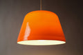 Front view of 1970s dual-layer orange and white acrylic Space Age pendant lamp, showing the clean dome silhouette with white interior, softly illuminated.