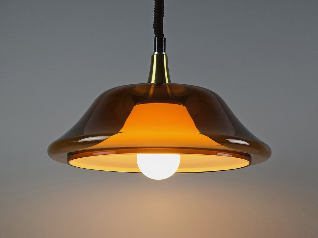 Vintage 1970s amber acrylic UFO pendant light illuminated, showing a warm glow through the translucent Space Age shade.