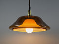 Vintage 1970s amber acrylic UFO pendant light illuminated, showing a warm glow through the translucent Space Age shade.