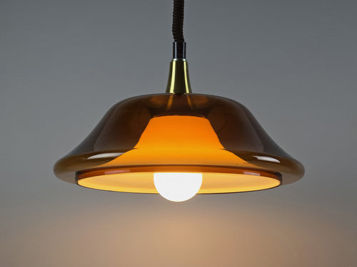 Vintage 1970s amber acrylic UFO pendant light illuminated, showing a warm glow through the translucent Space Age shade.