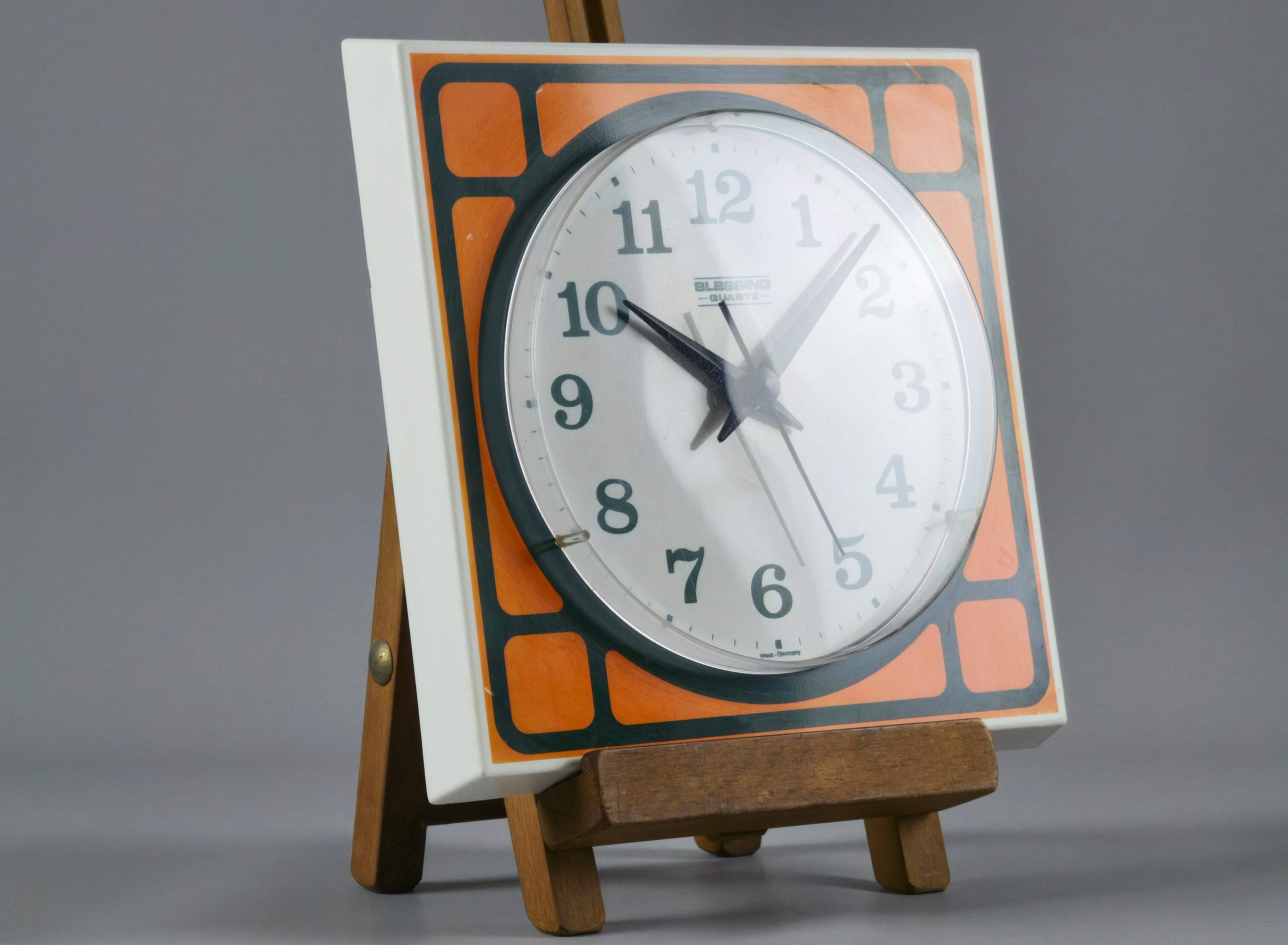 1970s Space-Age Design Blessing orange plastic wall clock, on a wooden stand with a projector partially hitting the clear plastic face.