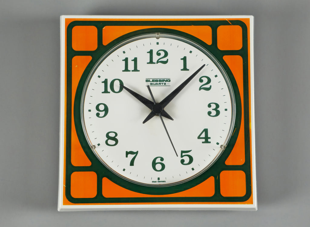 1970s Space-Age Design Blessing orange plastic wall clock, front view on a light grey background showing the orange and forest green face design.