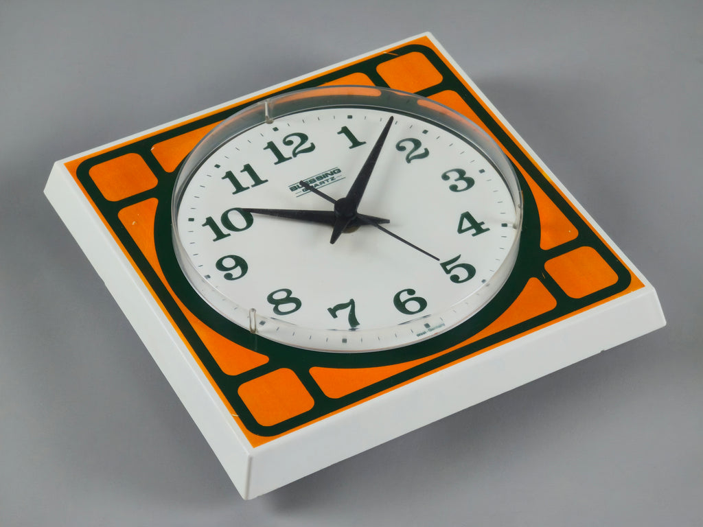 1970s Space-Age Design Blessing orange plastic wall clock, laid down on a neutral background showing a different angle.