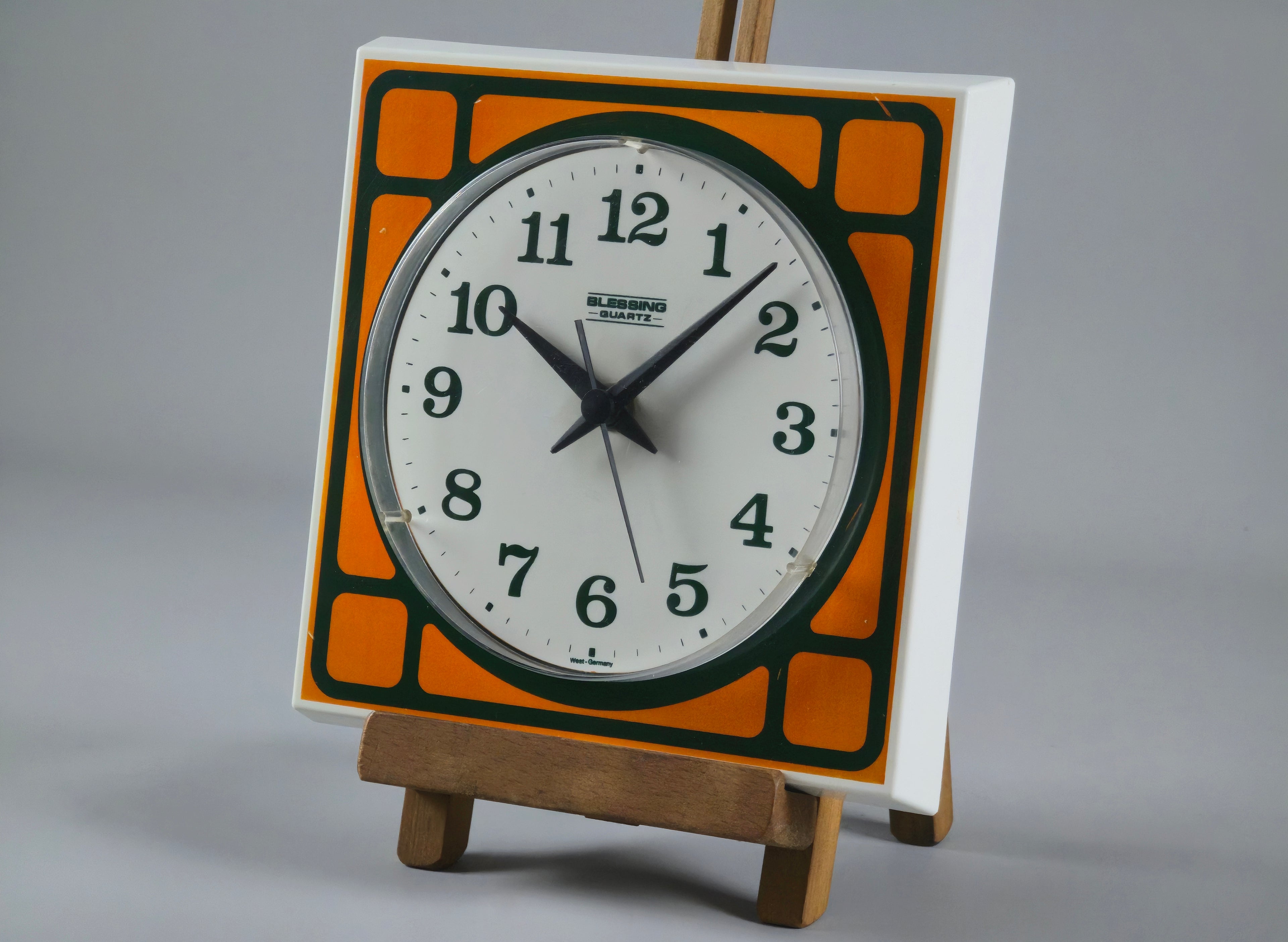 1970s Space-Age Design Blessing orange plastic wall clock, angled profile of clock on a vintage wooden stand.