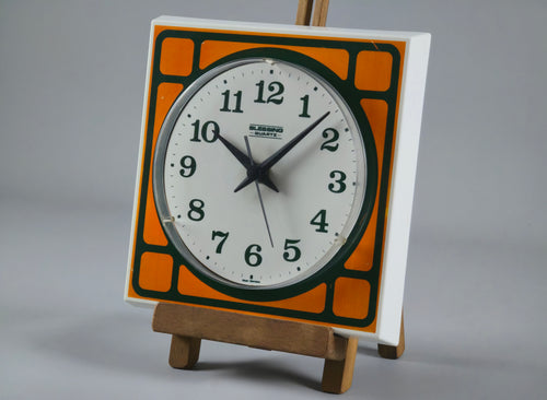 1970s Space-Age Design Blessing orange plastic wall clock, angled profile of clock on a vintage wooden stand.