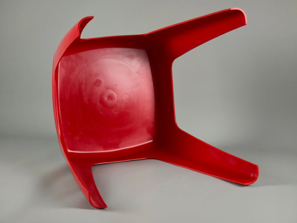 Close-up of the underside of the red stool showing the embossed "Flair Holland" manufacturer's mark and "Made in Holland" stamp on the red molded plastic surface.