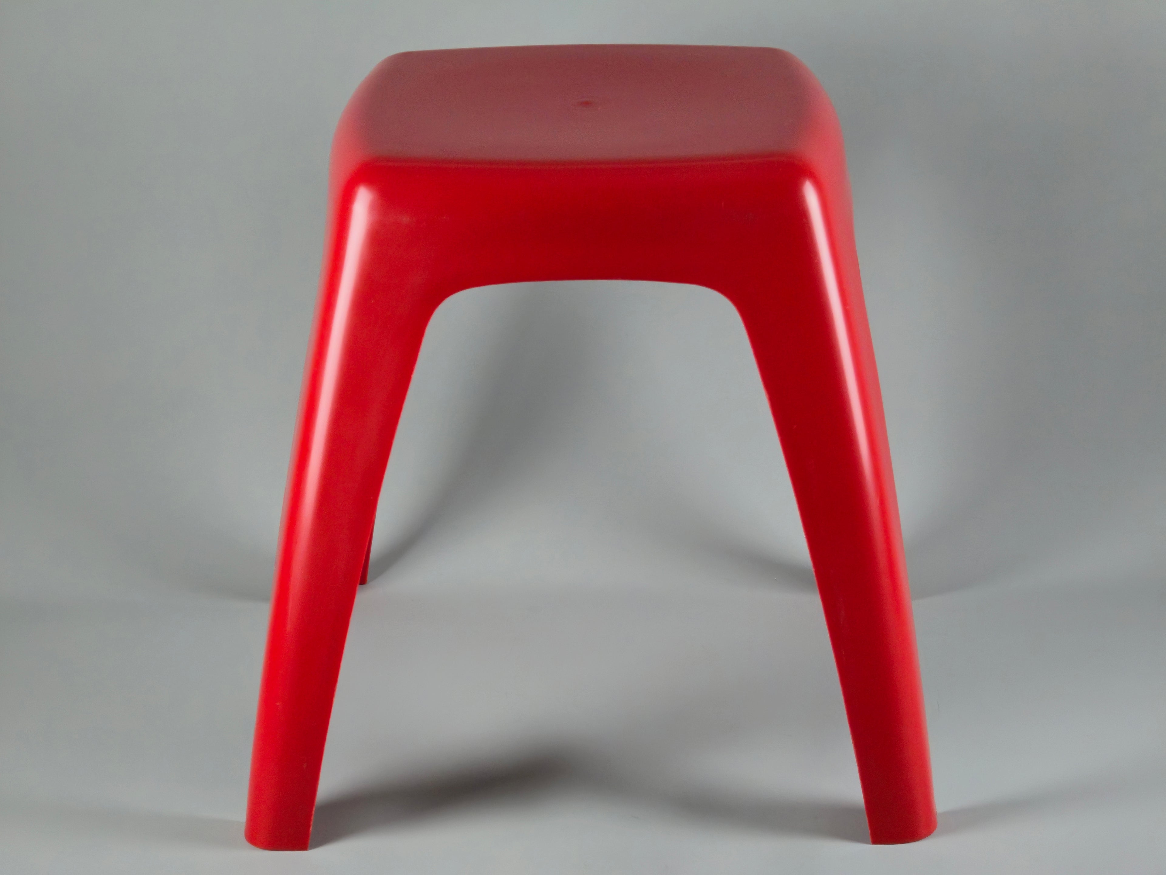 Bird's eye view of the rounded square red seat of the stool. The glossy ABS plastic surface shows a bright, reflective shine with no visible cracks or damage.