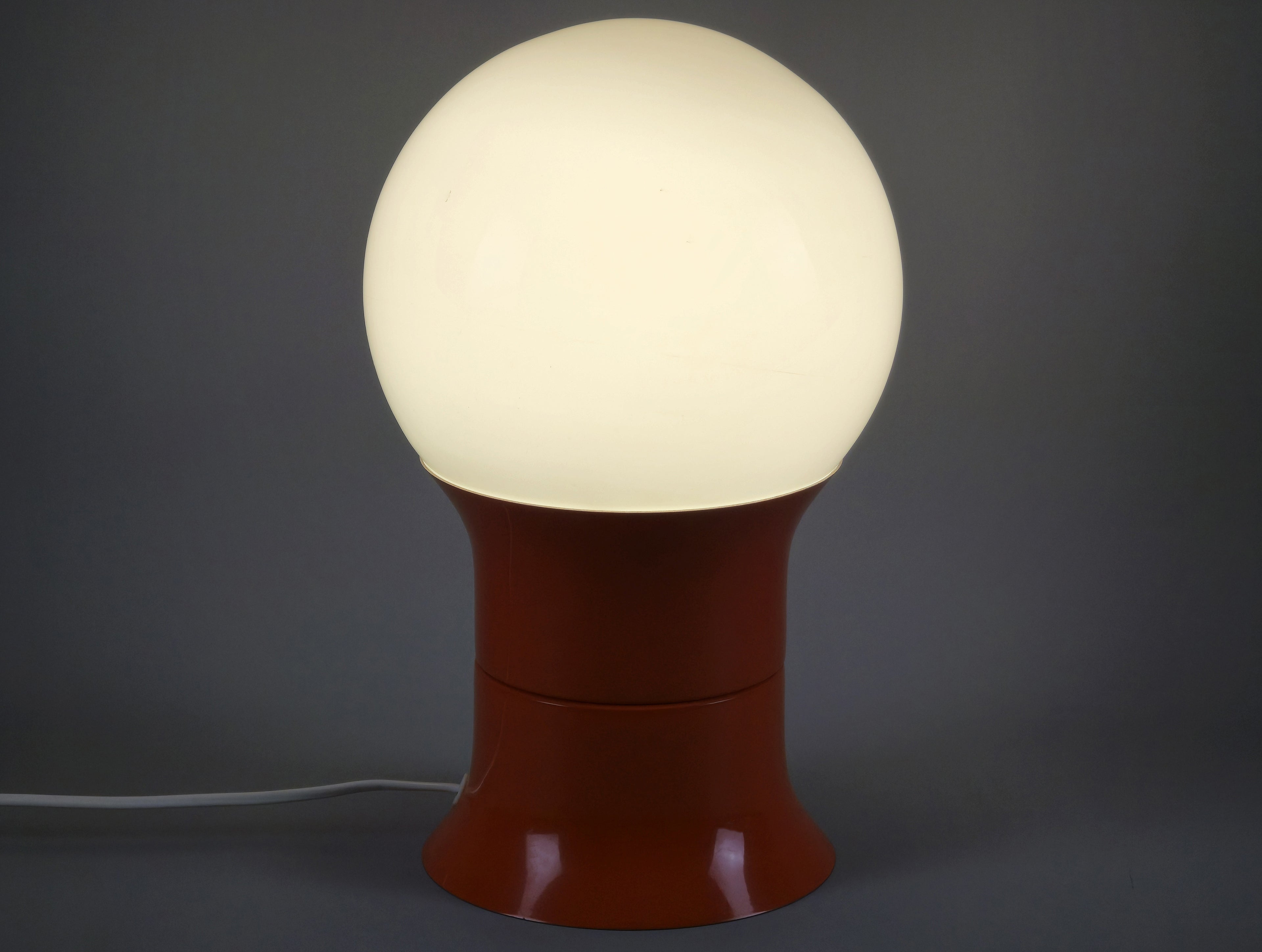 1971 Space age design 'HEMI Klot 2' table lamp by Lennart Centervall, with opaline glass ball shade and orange lacquered base, front view and amber lit, slightly angled view from the front side.