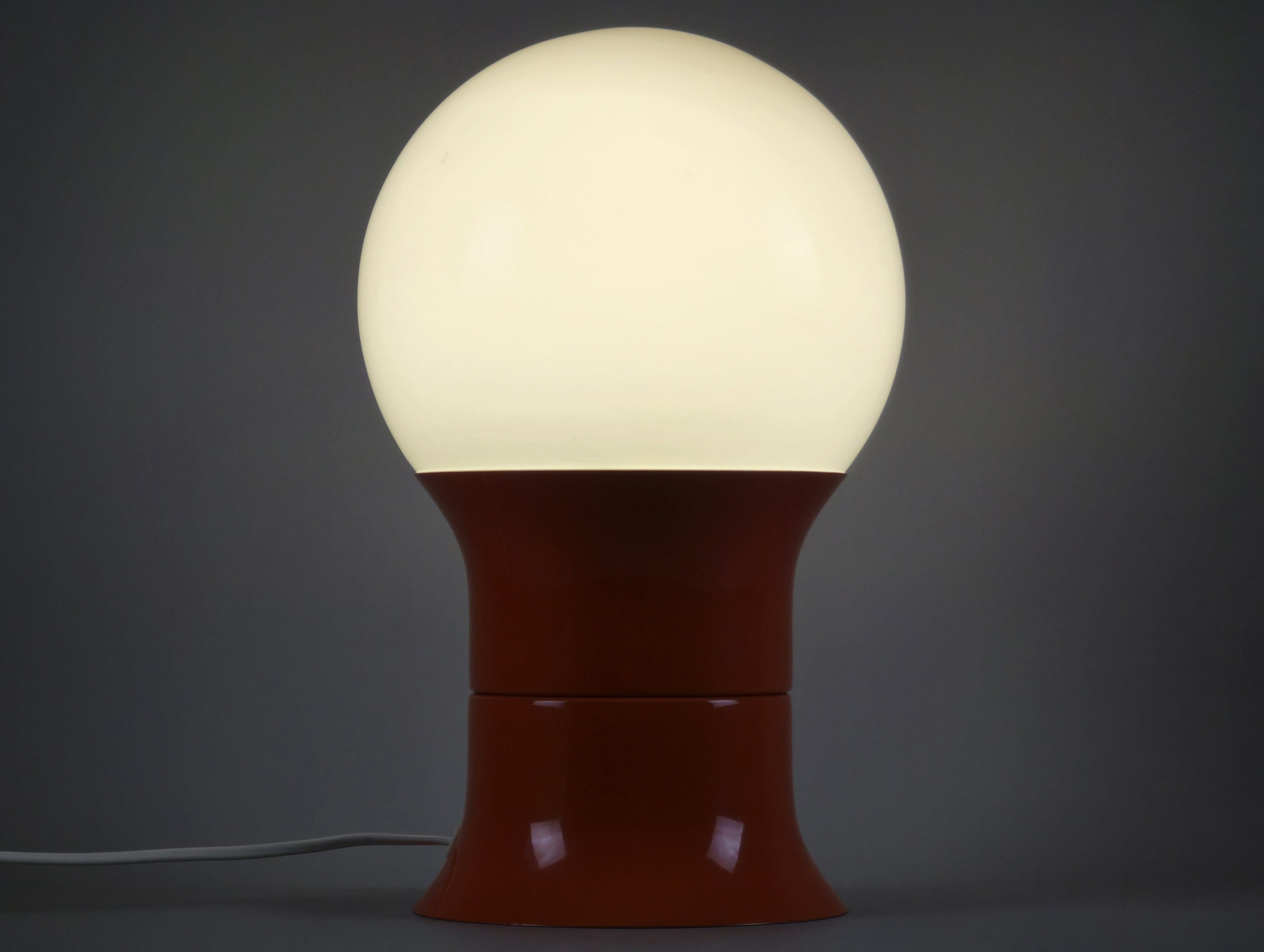 1971 Space age design 'HEMI Klot 2' table lamp by Lennart Centervall, with opaline glass ball shade and orange lacquered base, front view and amber lit showing the glow of the ball shade.