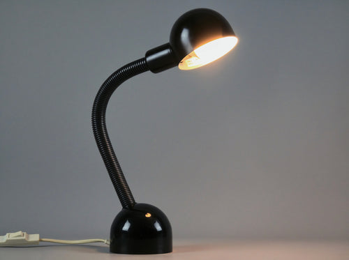 Vintage Happylight Holland desk lamp illuminated, showing a warm, directed task light glow against a neutral studio background.