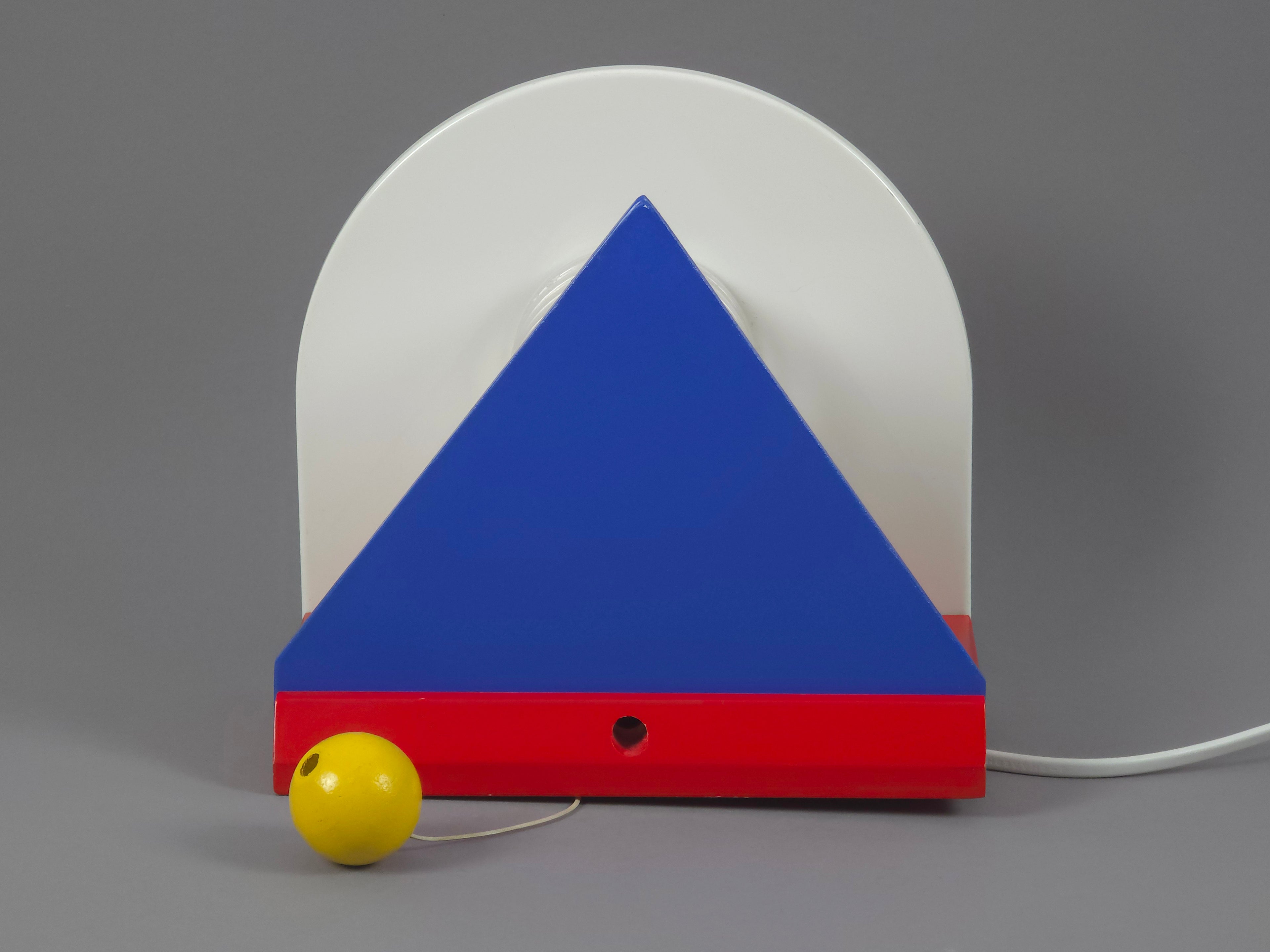 1987 Vintage IKEA V716 Stoja wall lamp front view showing the blue triangle, red trim, white semi-circular backplate and yellow ball.