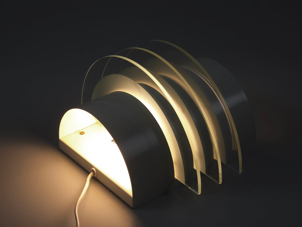 IKEA Drittel wall lamp illuminated, angular shot laid on its back showing the warm tiered light wash against a neutral wall.