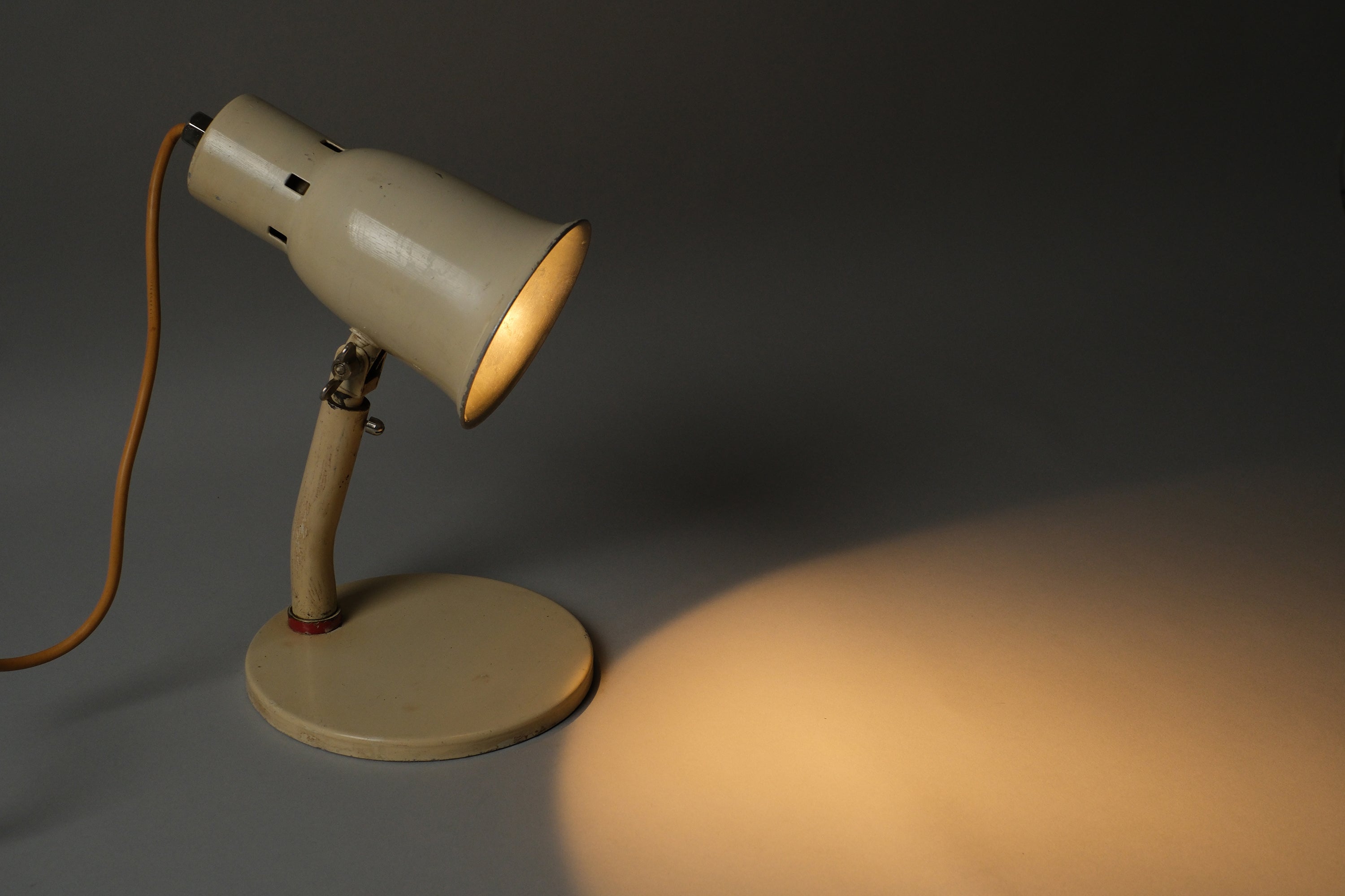 Top-down illuminated view of a 1920s-1930s Bauhaus industrial desk lamp, Kandem type, showing directional light cast downward from the cream enamel shade onto the surface below.