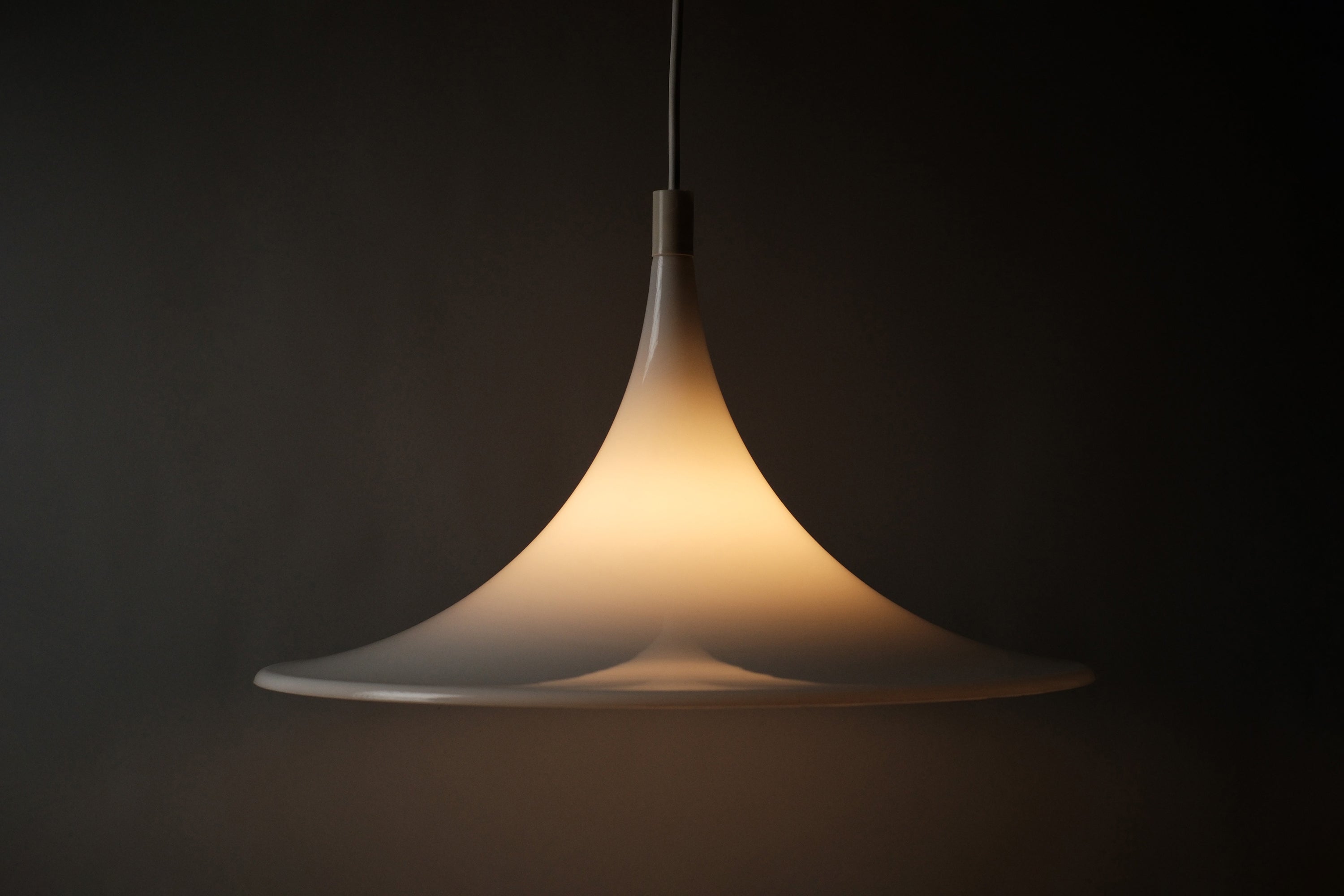 Profile view of the Dijkstra witch hat pendant fully illuminated, warm opaline glow revealing the shade's translucent depth