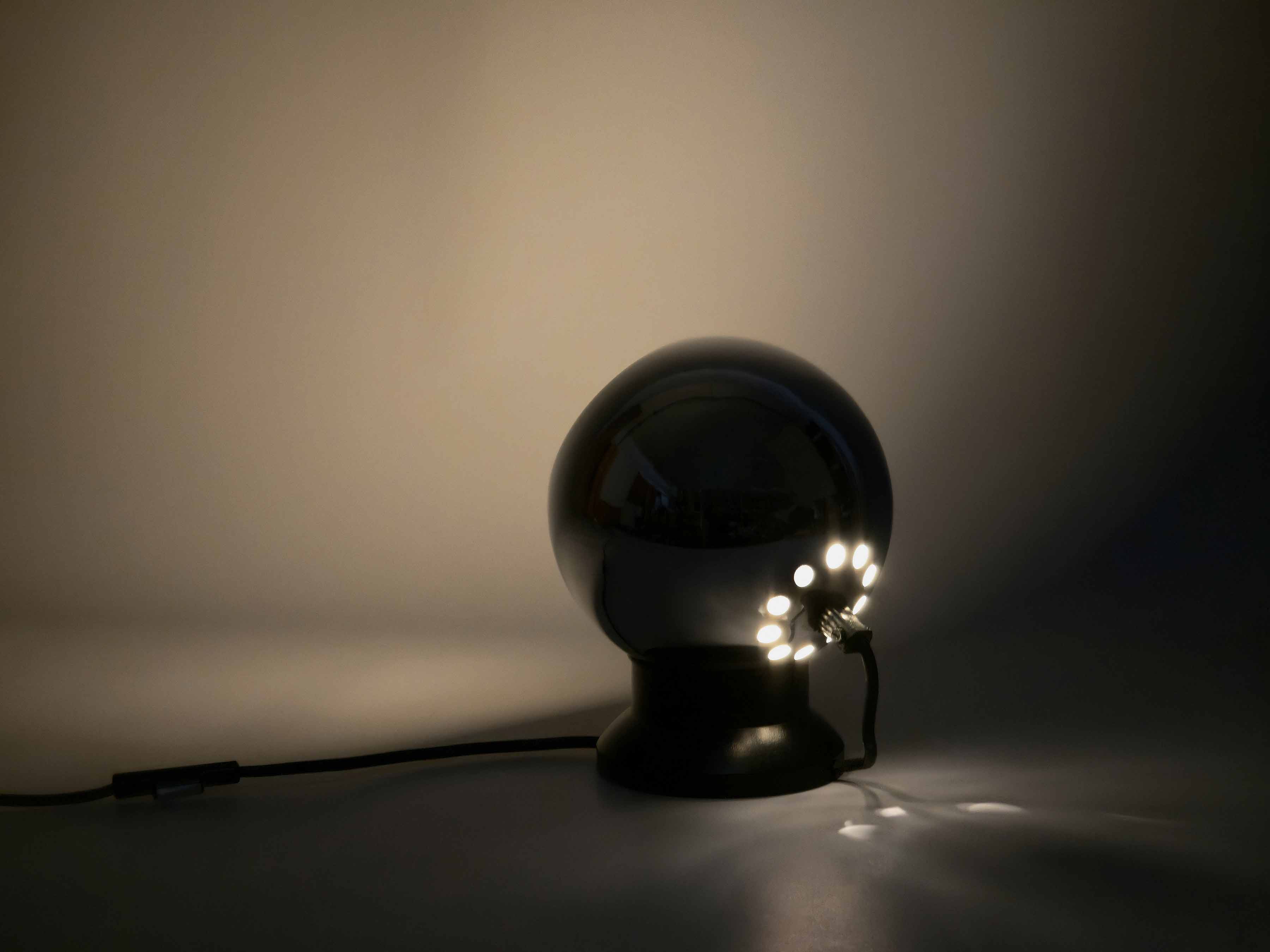 Angled view from the back and lit in dark room of the vintage 1970s E.S. Horn magnetic ball lamp. The lamp casts its light on a wall showing the projection.