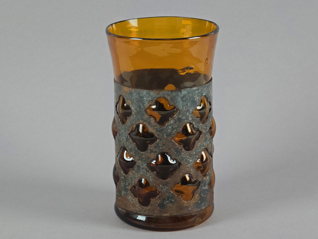 Single view of a Derflingher amber glass tumbler highlighting the geometric metal cutout design.