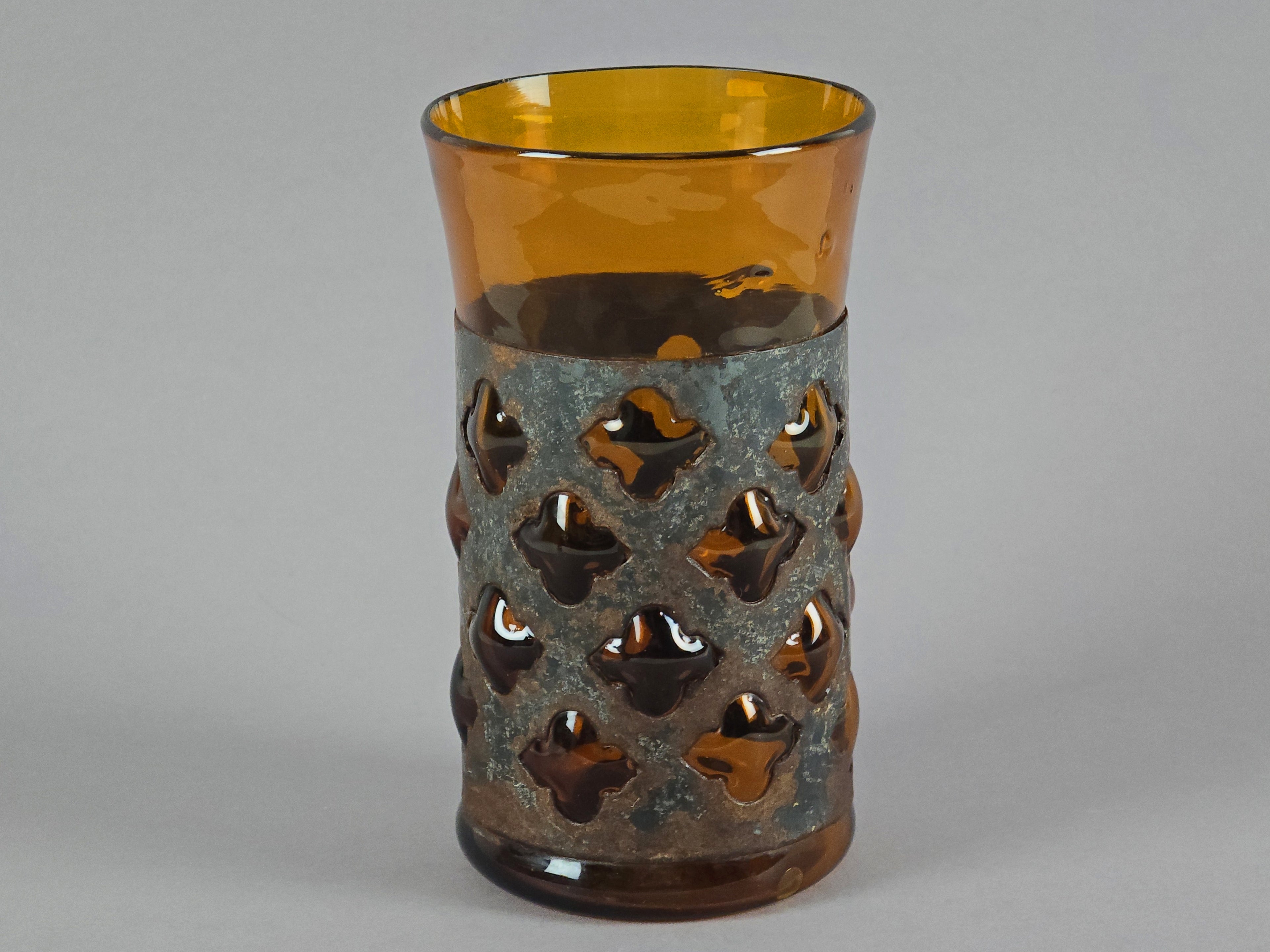 Single view of a Derflingher amber glass tumbler highlighting the geometric metal cutout design.
