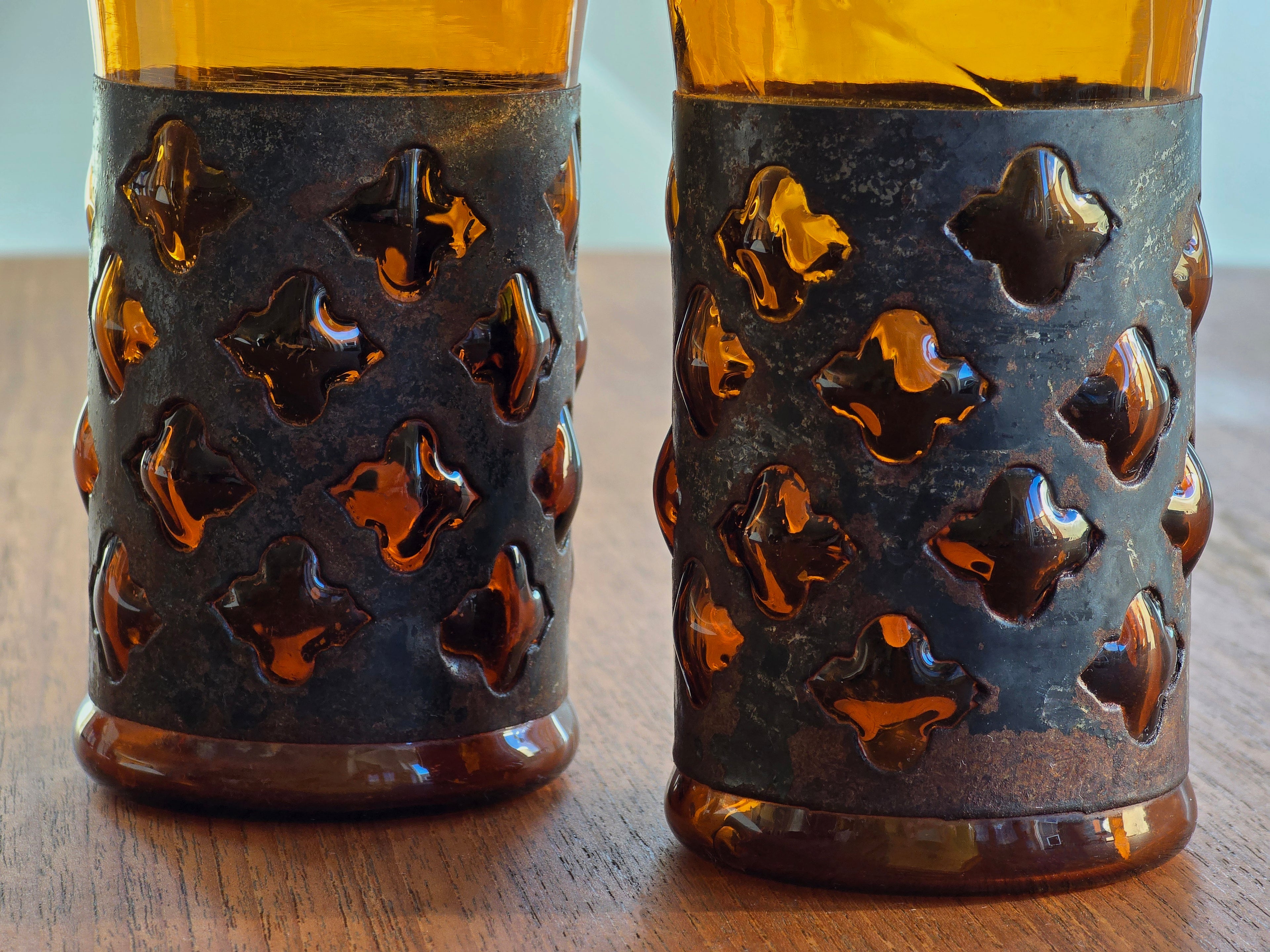 Close-up texture shot of hand-blown amber glass bulging through a brutalist metal frame.