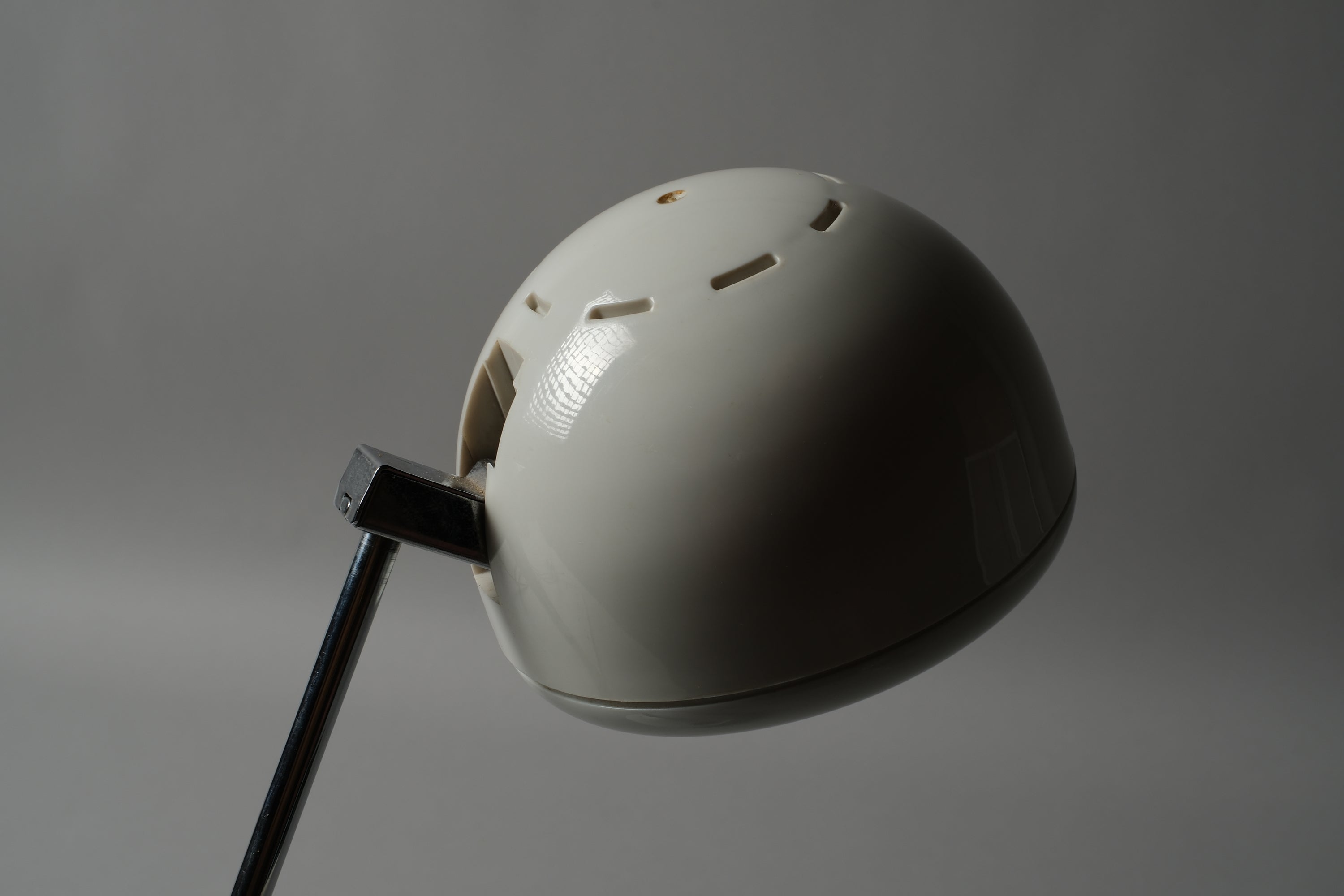 Macro detail of the spherical halogen spot head of a 1970s Hustadt Leuchten antenna desk lamp from West Germany, showing the rotating cup shade and ventilation slots on the white lacquered steel sphere.