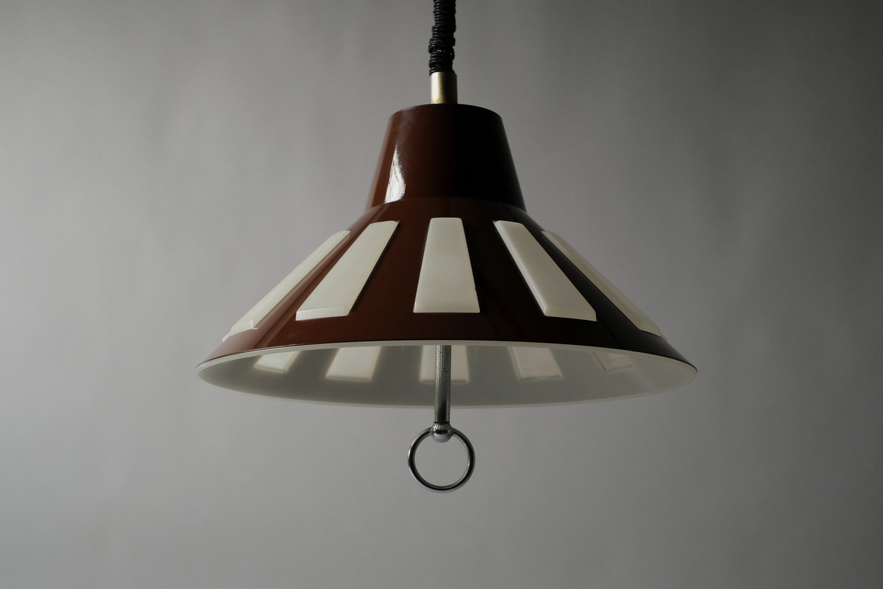 Low-angle view of a 1970s Massive Lighting Belgium UFO pendant lamp, showing the broad flared form and the translucent inner layer visible through the geometric cutouts in the brown outer shell.