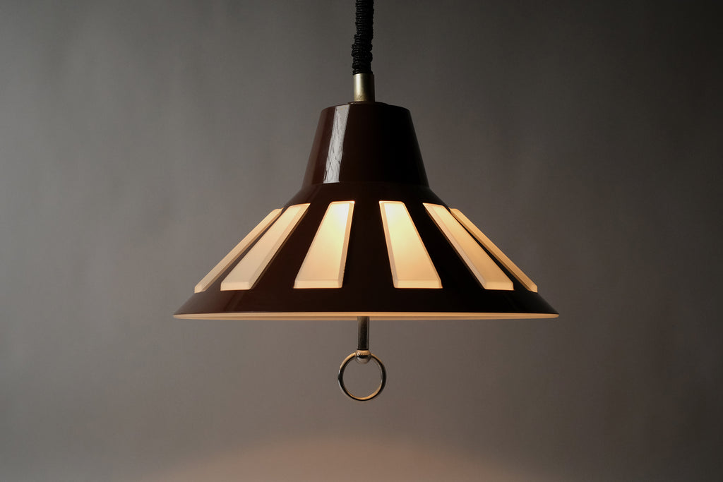 Profile illuminated view of a 1970s Massive Lighting Belgium UFO pendant lamp, showing the full silhouette and the warm striped glow produced by light passing through the geometric cutouts.