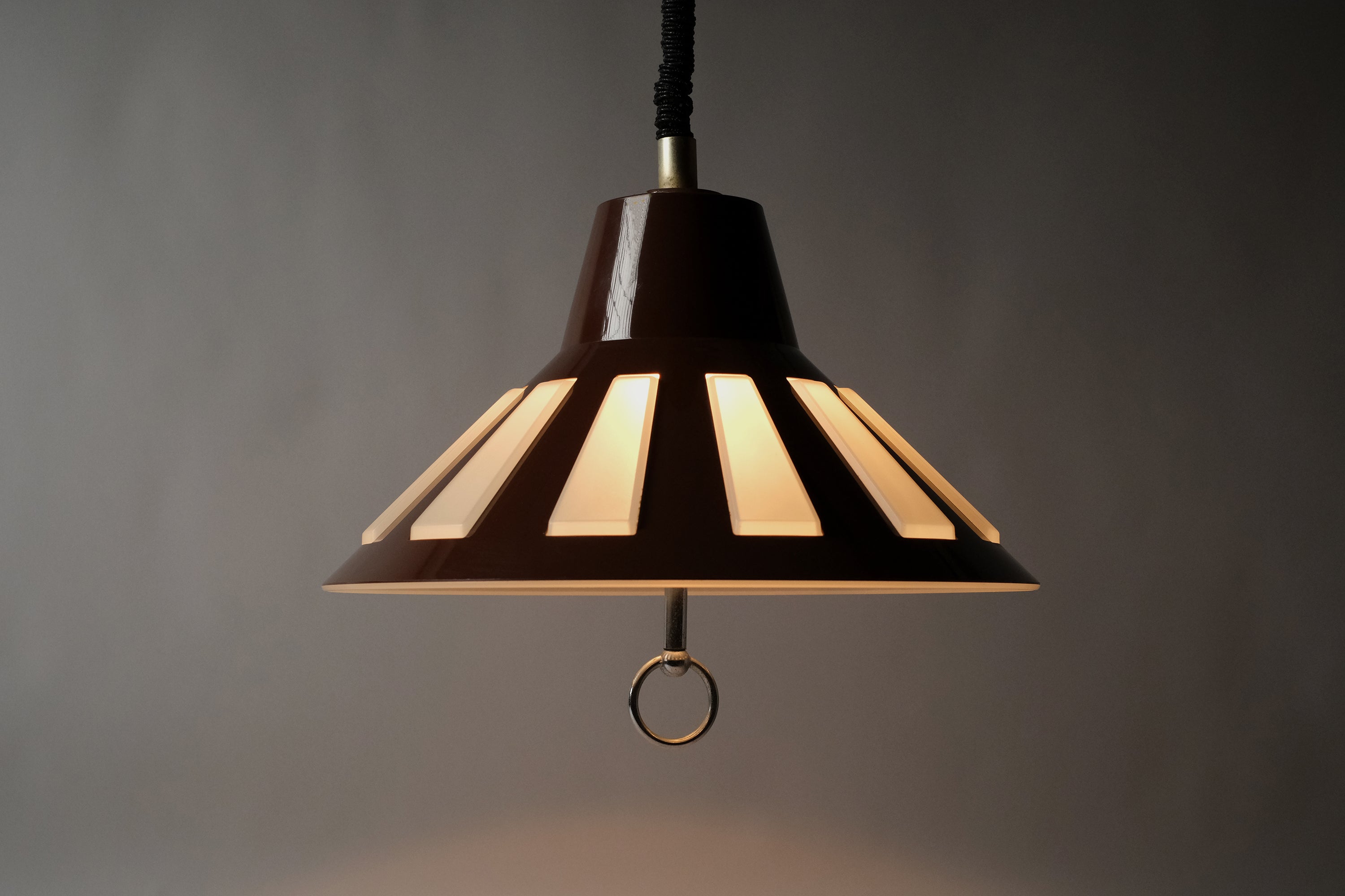 Profile illuminated view of a 1970s Massive Lighting Belgium UFO pendant lamp, showing the full silhouette and the warm striped glow produced by light passing through the geometric cutouts.