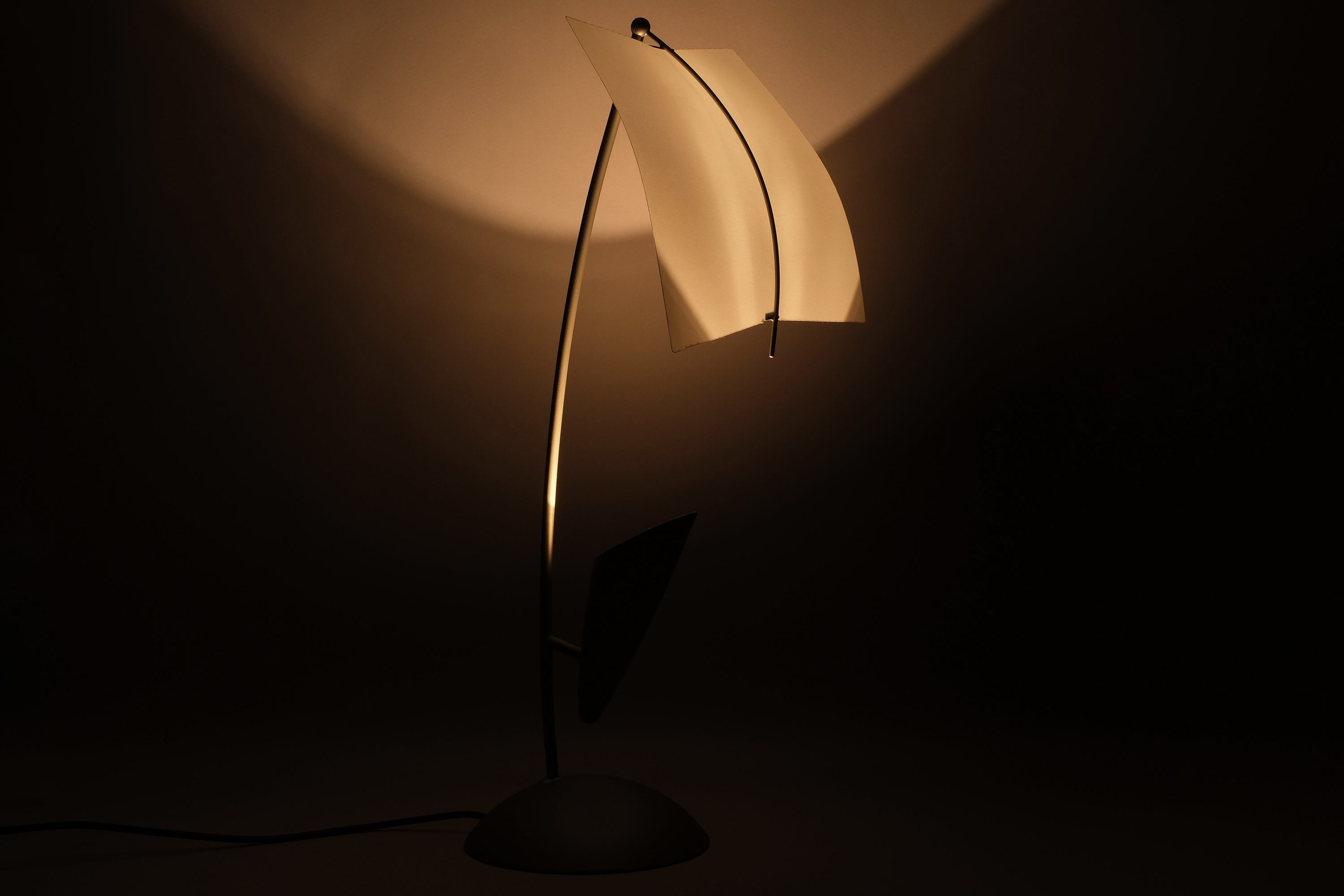 Front illuminated view of a Rolf Benz Nuvola table lamp, Art. Nr. 79101009, showing warm halogen light distributed across the curved white lacquered steel diffuser, Germany.