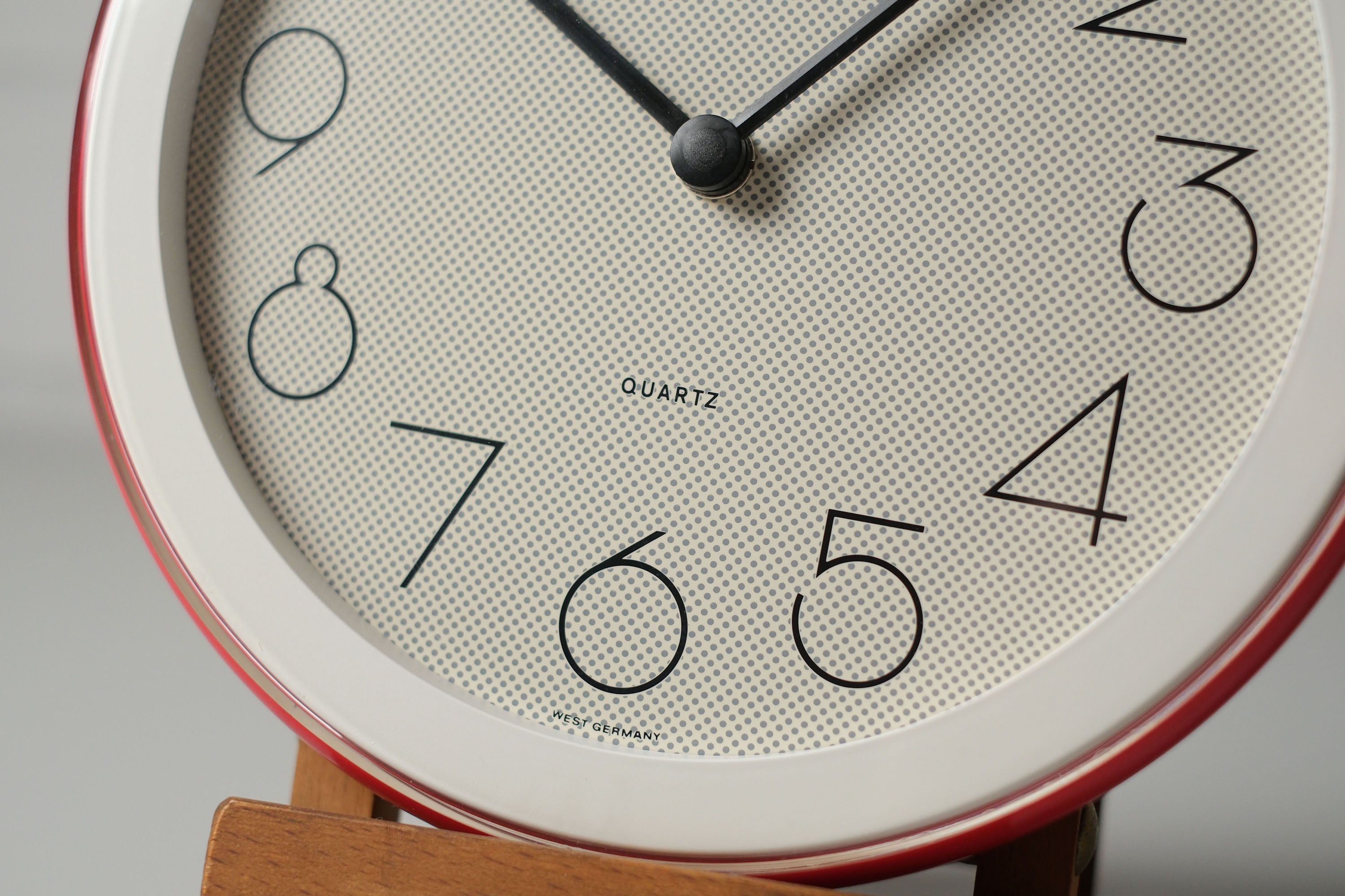 Close-up detail image of the bottom half of vintage 1980s postmodern round wall clock by Staiger West Germany with pop-art dotted face, red and white plastic frame.