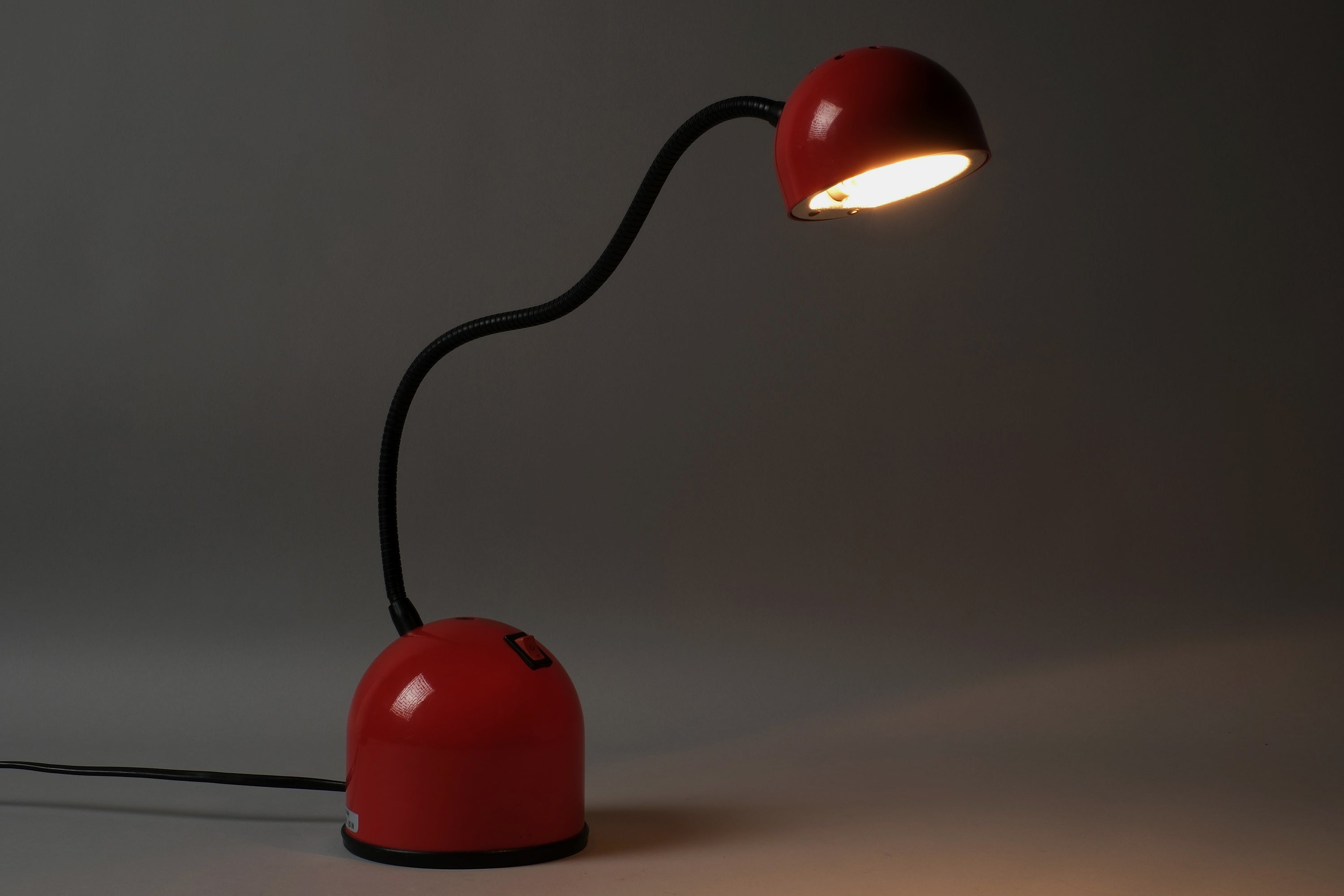 Illuminated view of a 1980s Stilplast flexible halogen desk lamp from Italy, showing the warm directional halogen light cast from the adjustable spot head on the black gooseneck arm.