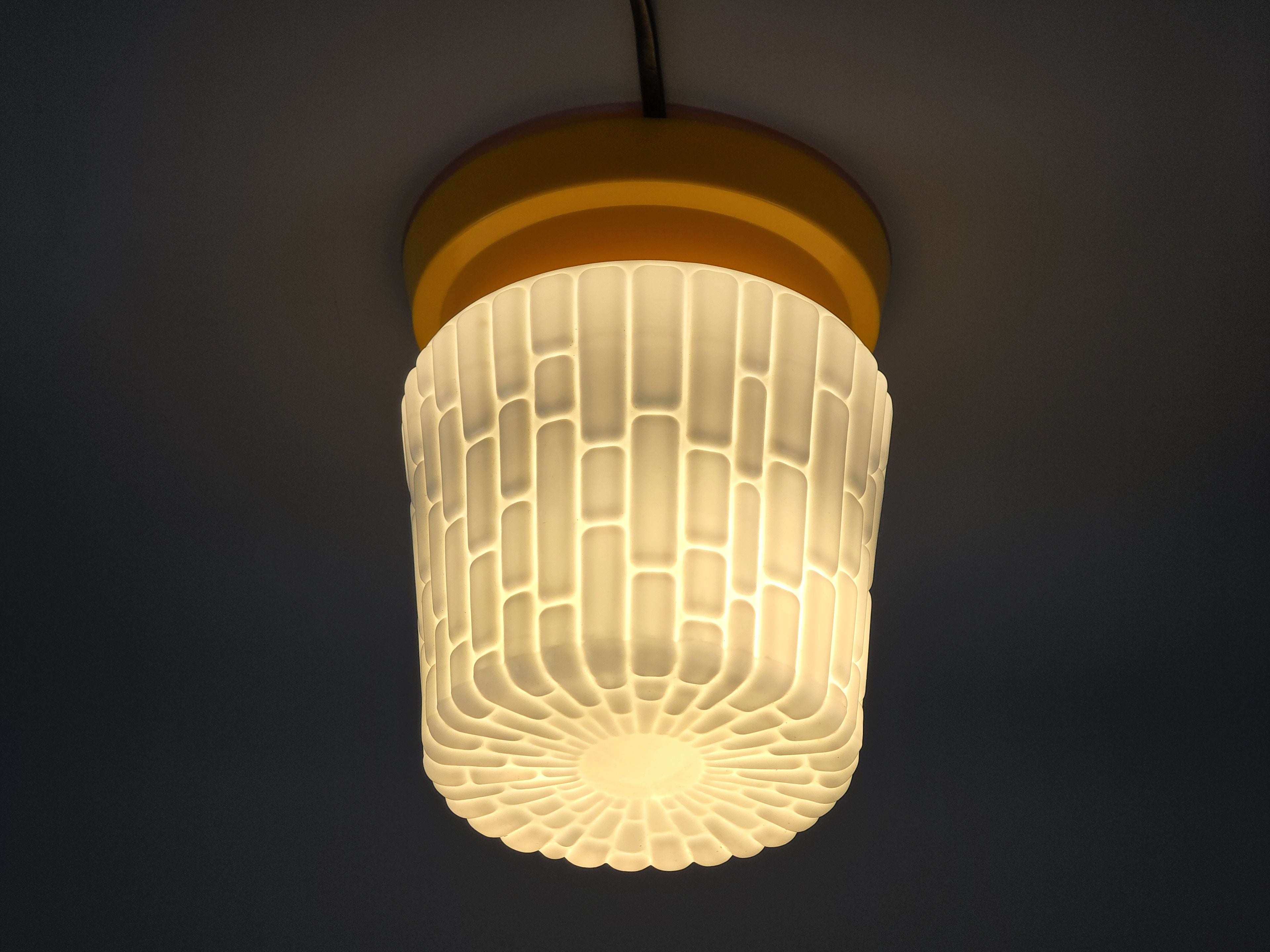 Vintage yellow ceiling light illuminated, showing a warm amber glow through the textured white glass shade.