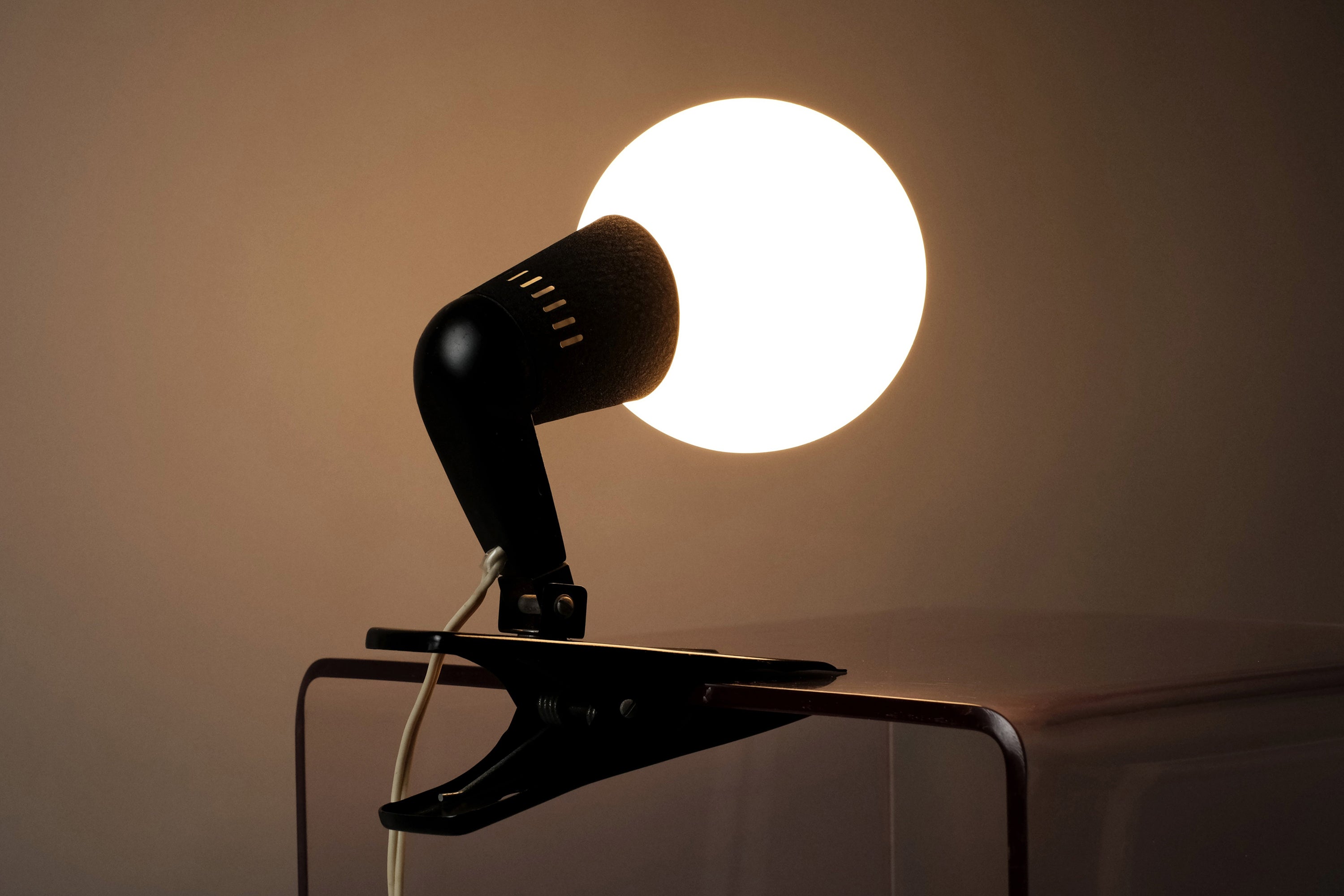 An illuminated rear-facing shot of the vintage 1960s ERCO MCM clamp spotlight German industrial clip-on desk lamp emphasizing its ambient glow.