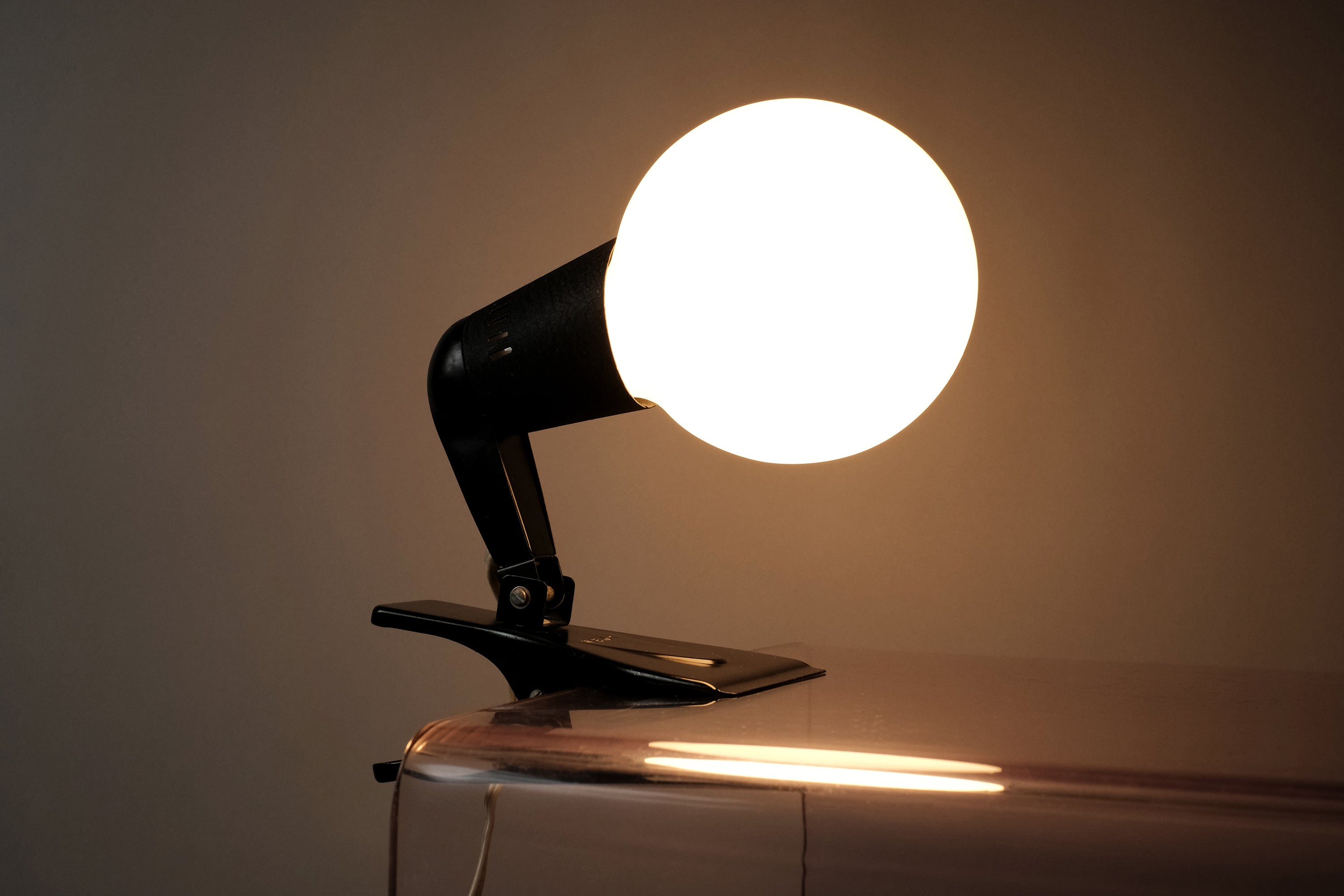 Primary illuminated shot of the vintage 1960s ERCO MCM clamp spotlight German industrial clip-on desk lamp attached to a clear acrylic shelf.