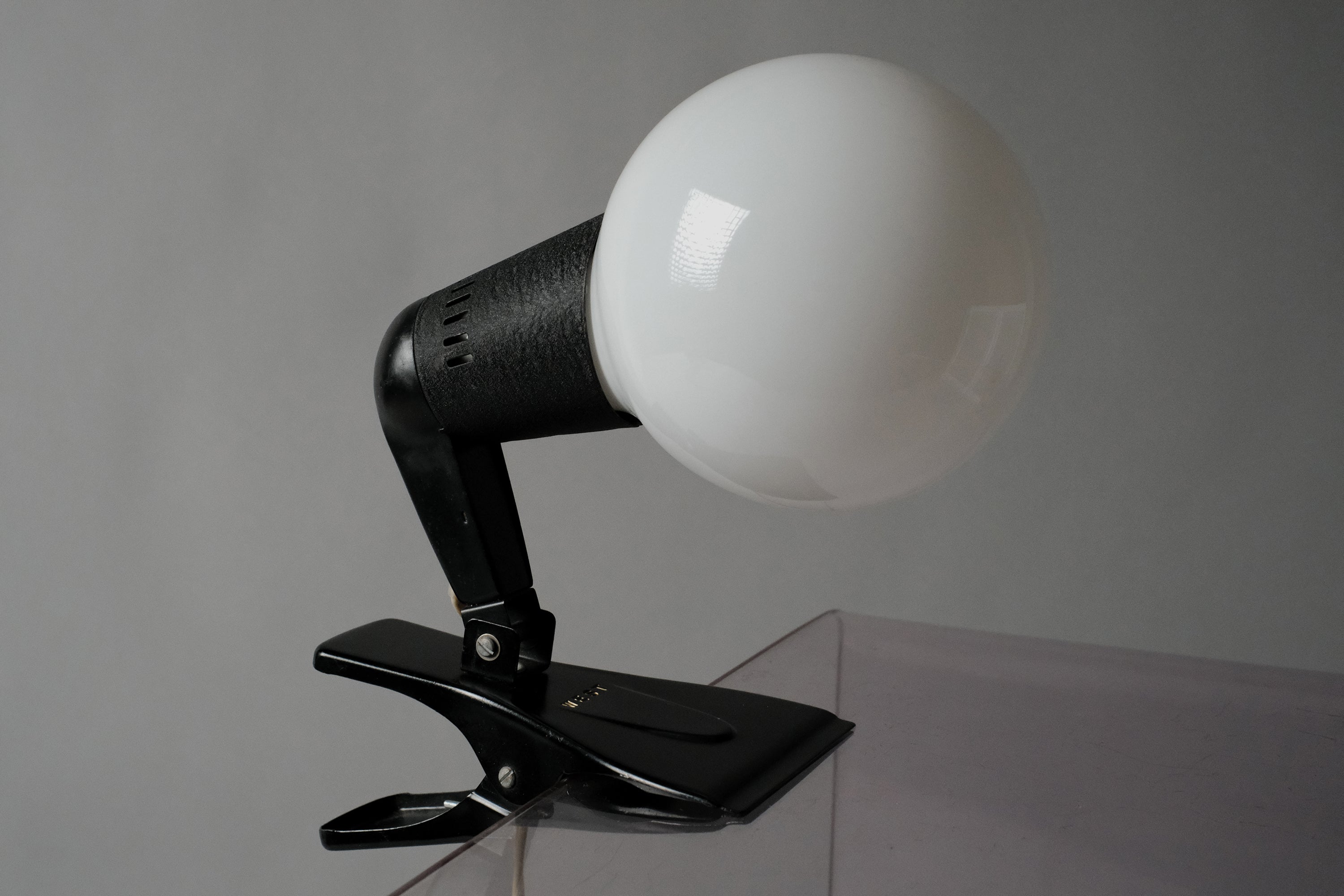 A profile view of the vintage 1960s ERCO MCM clamp spotlight German industrial clip-on desk lamp showing the black adjustable neck and globe bulb.