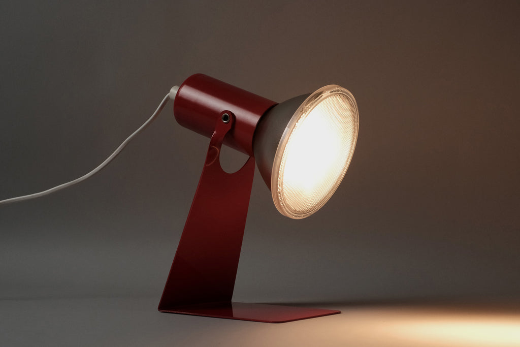 The vintage 1970s Gnosjo Konstsmide Swedish MCM red metal industrial desk lamp illuminated to show the direct task lighting beam.