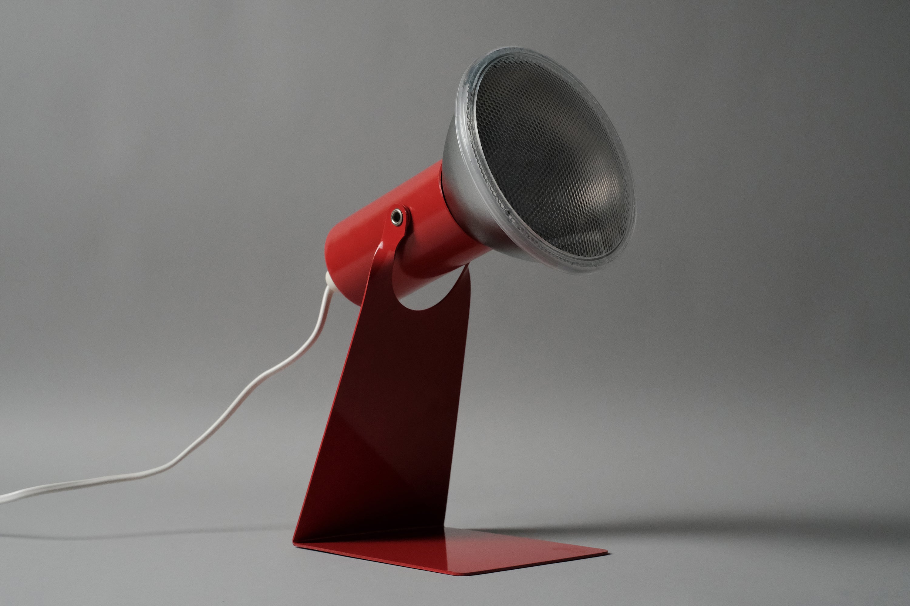 A profile view of the vintage 1970s Gnosjo Konstsmide Swedish MCM red metal industrial desk lamp highlighting the sleek angled neck.