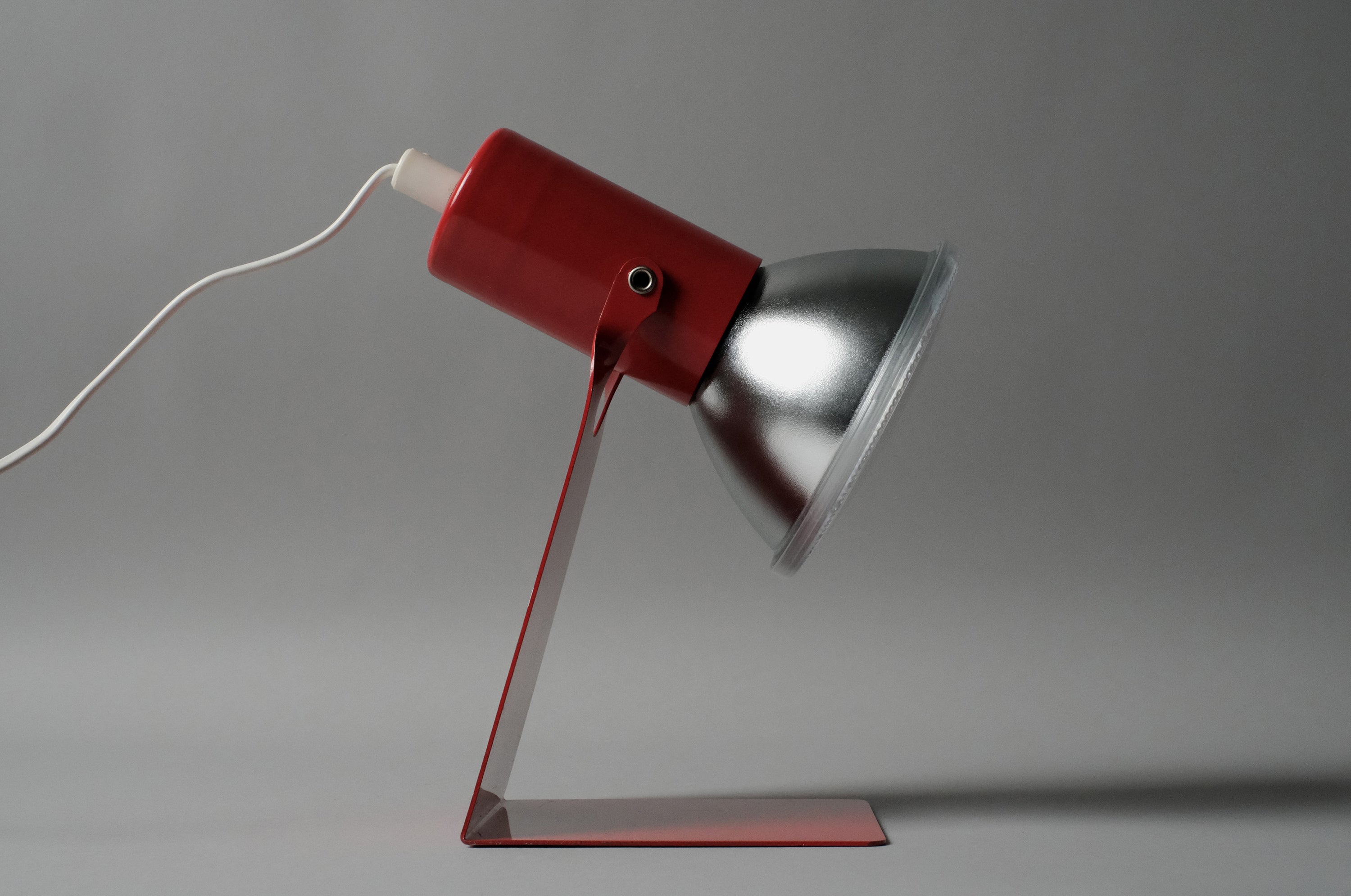 A side profile shot of the vintage 1970s Gnosjo Konstsmide Swedish MCM red metal industrial desk lamp focusing on the reflector bulb.