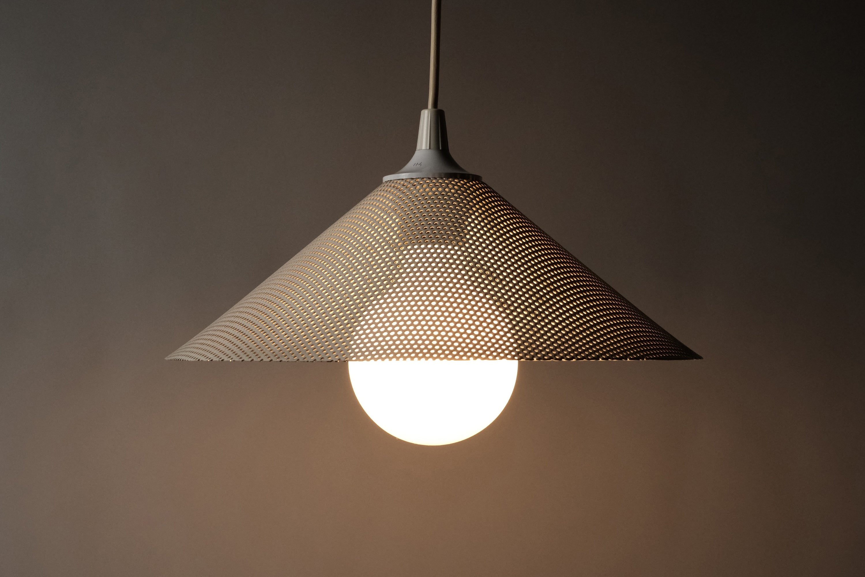 Herda pendant lamp profile view illuminated, perforated metal light scatter softly with large E27 light bulb.