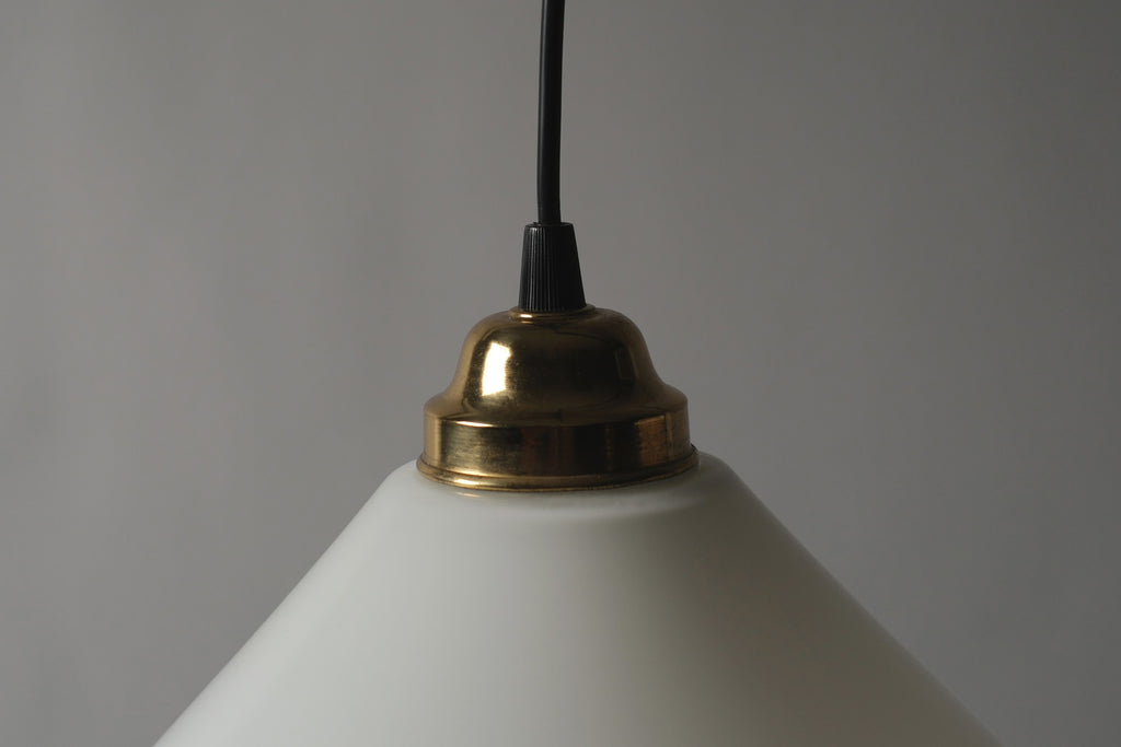 Close-up of the gold-plated brass fitting and black fabric cord of a 1980s vintage opal glass cone pendant lamp, showing the hardware detail against the ivory white glass shade.