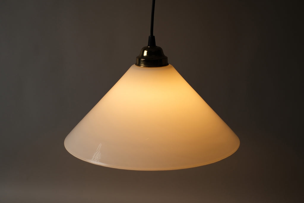 High-angle illuminated view of a 1980s vintage opal glass cone pendant lamp, showing the warm amber glow diffused evenly across the opaline glass surface when lit.